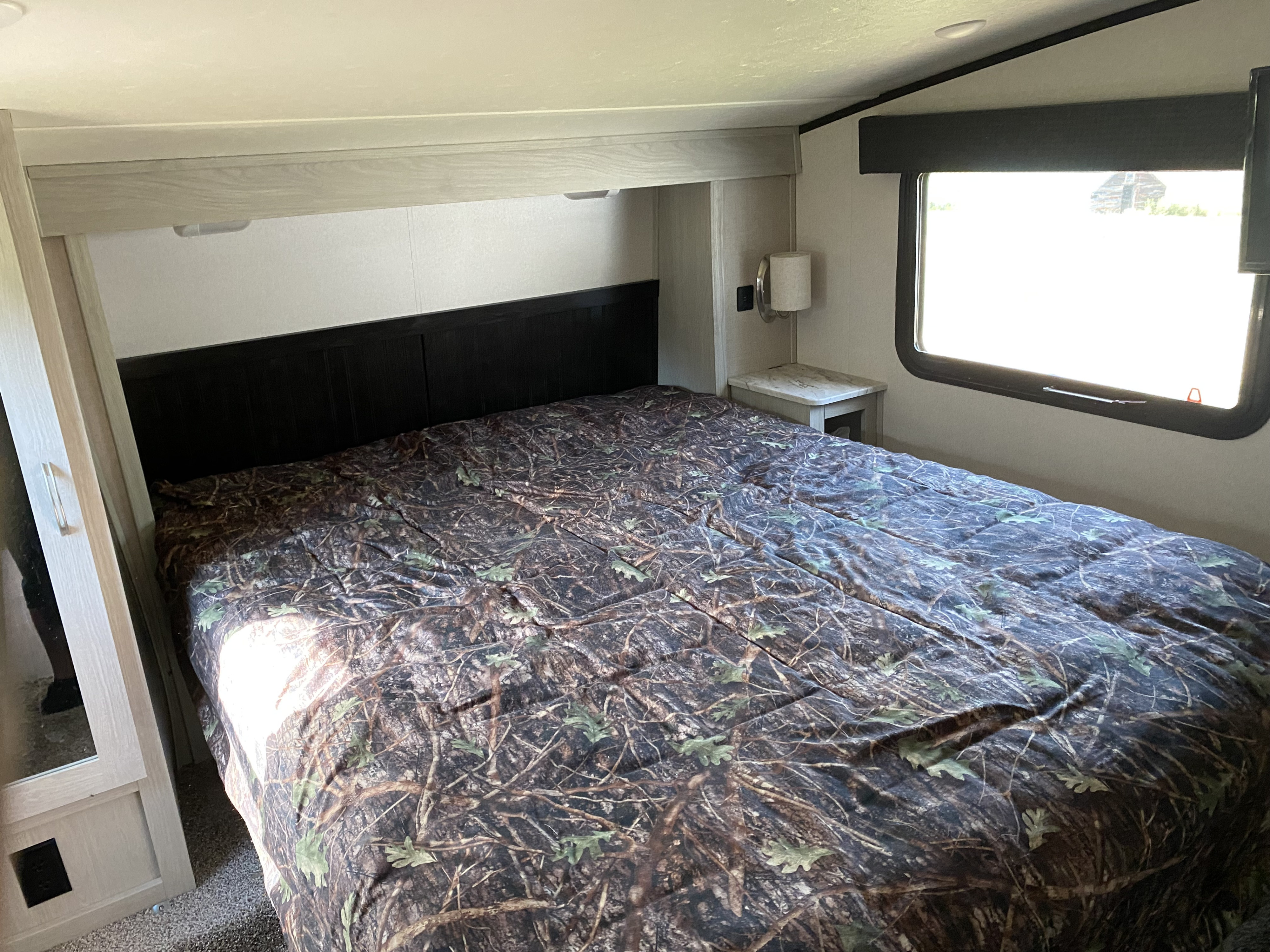 RV rental bedroom with a camouflage patterned bed, overhead storage, and a bedside lamp. Compact and cozy interior.. Forest River Coachmen Chaparral X-Lite 2018