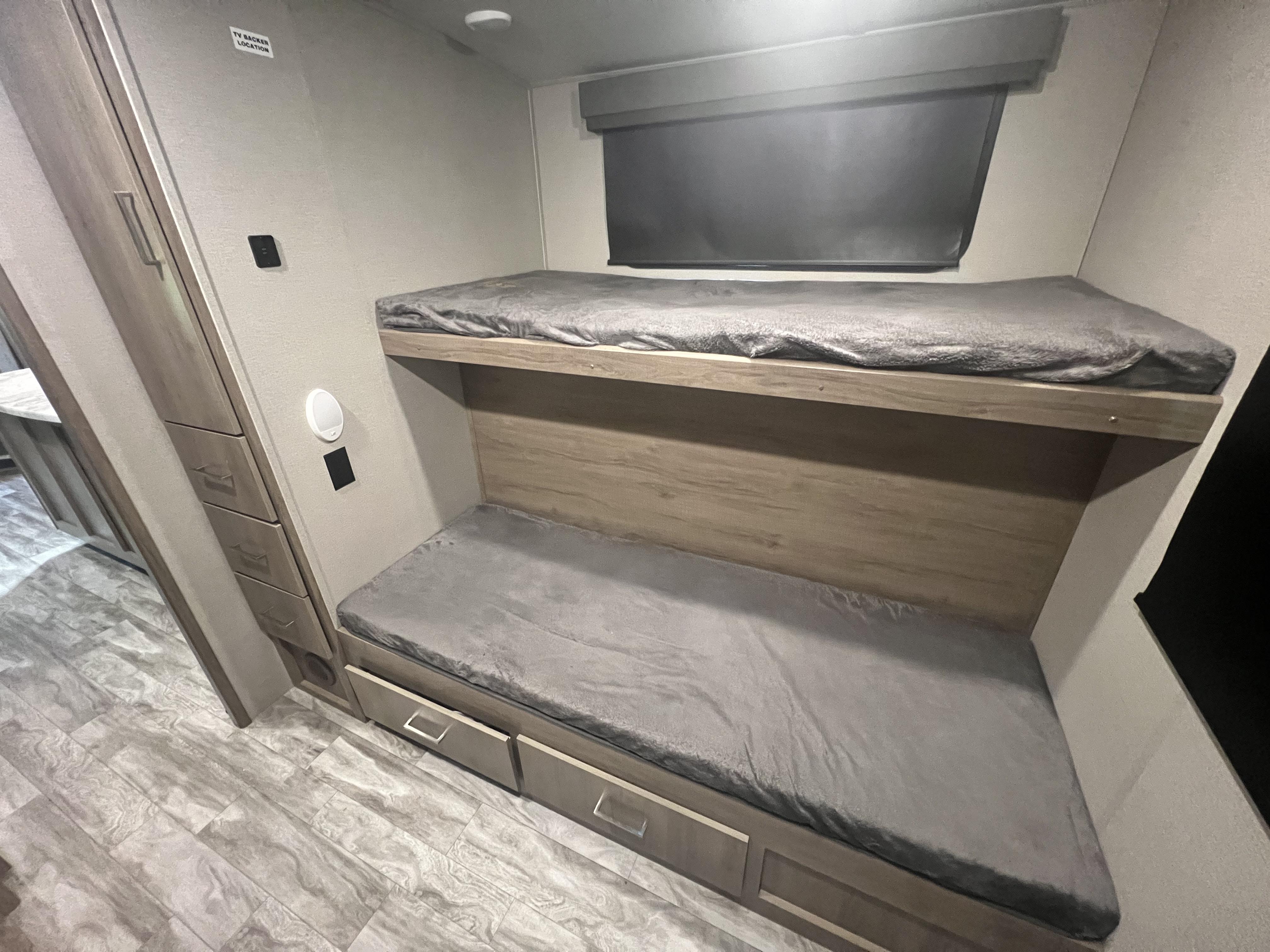 Interior of an RV rental showing modern bunk beds with grey mattresses, providing cozy sleeping space & storage.. Grand Design Imagine 2022