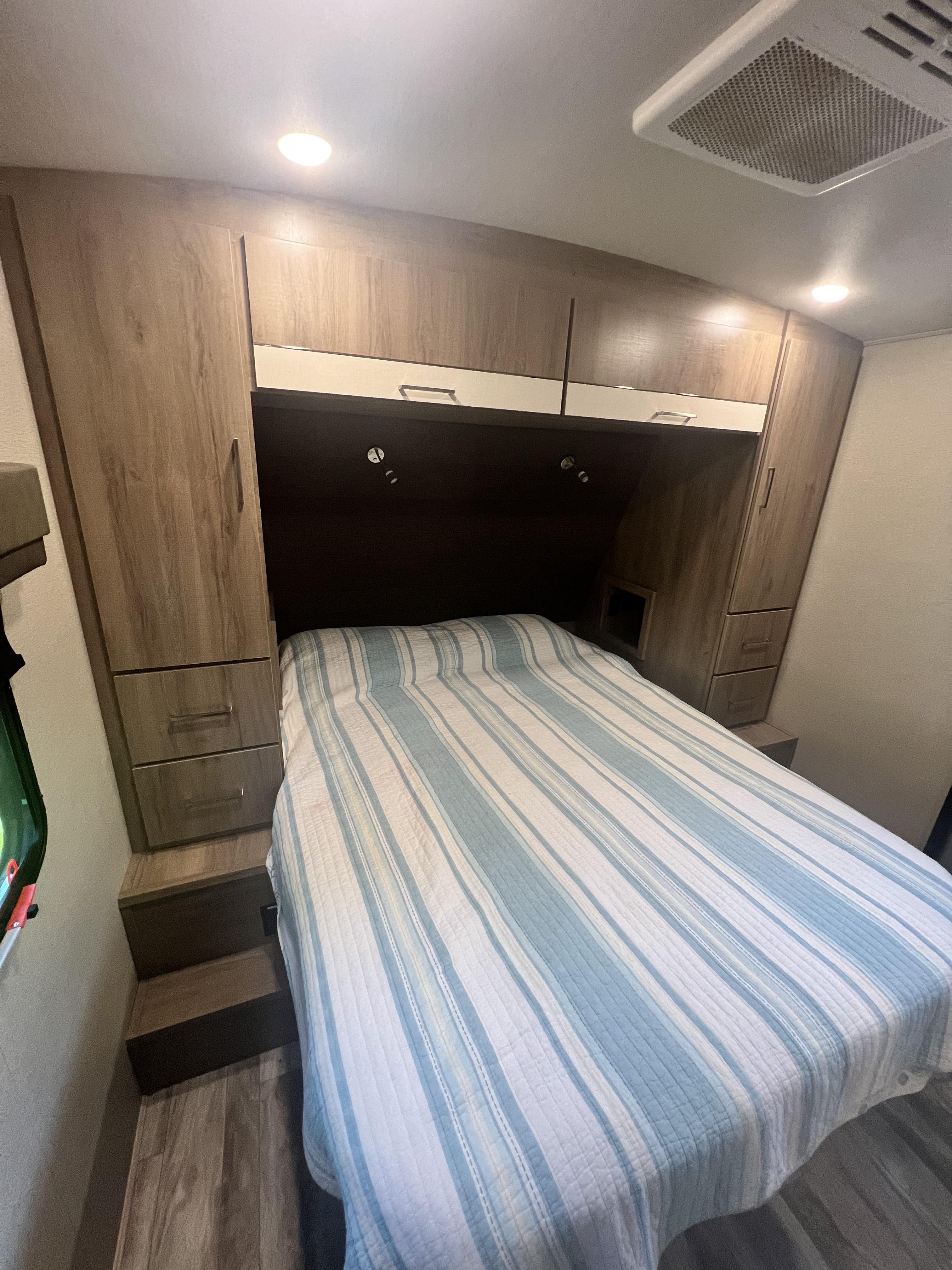 Cozy RV rental bedroom with a striped bed, built-in storage, and ceiling AC vent, ideal for compact comfort.. Grand Design Imagine 2022