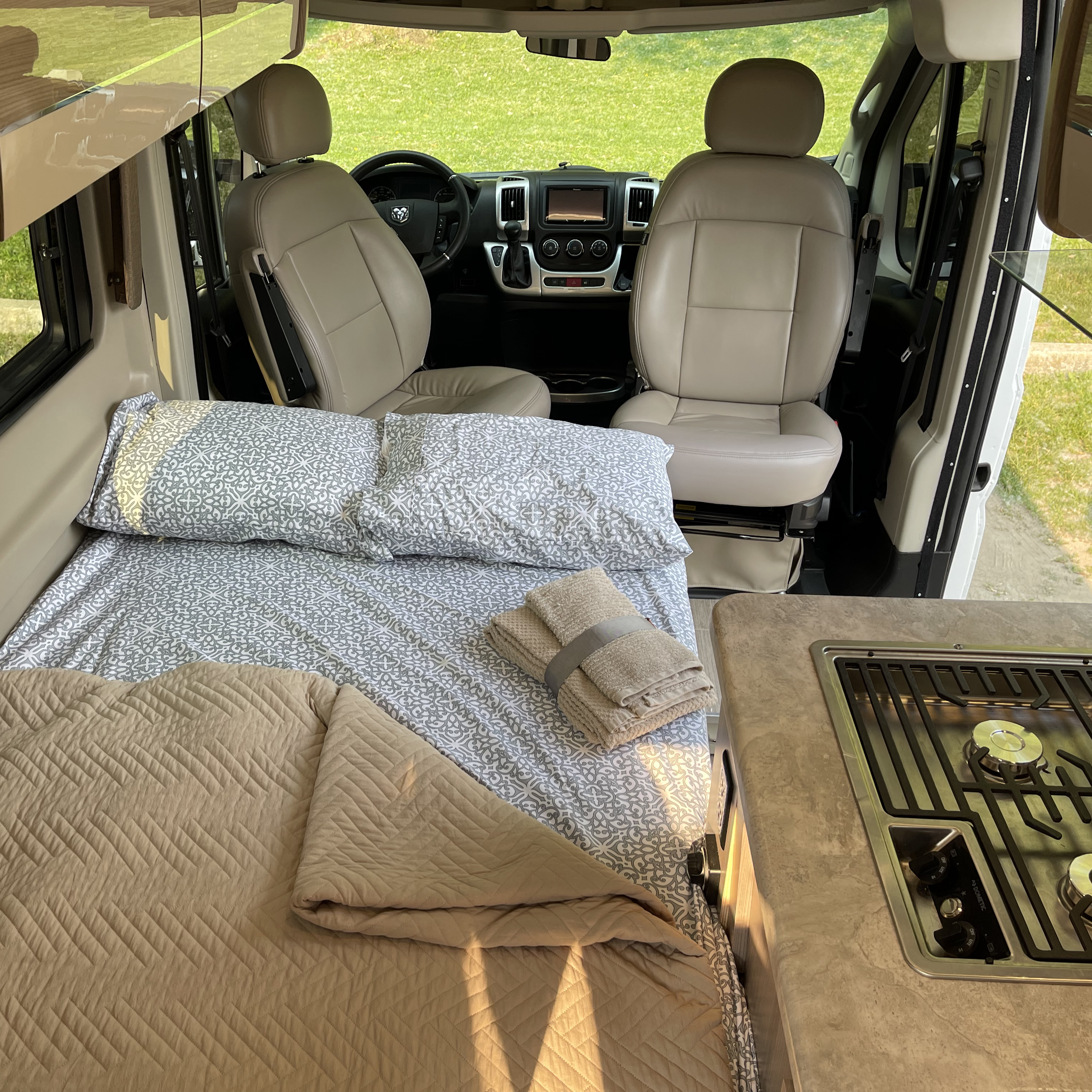 This RV rental interior features a comfortable bed with soft bedding, a compact kitchen with a stovetop, and the front driving cabin.. Thor Motor Coach Scope 2022