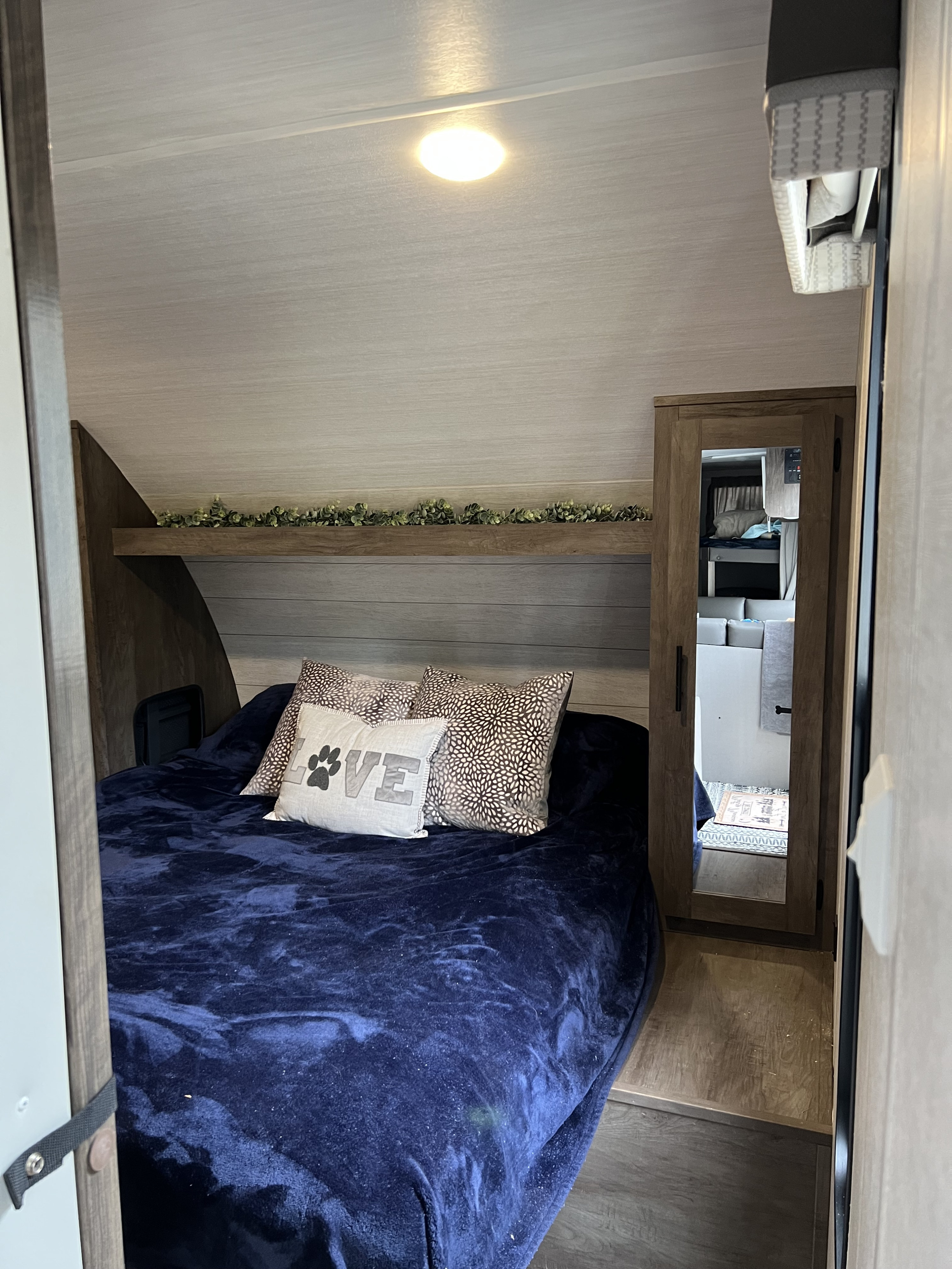 Enjoy a comfortable RV rental stay in this cozy bedroom featuring a blue bed, paw print pillow, and mirrored cabinet.. Forest River Wildwood X-Lite 2021