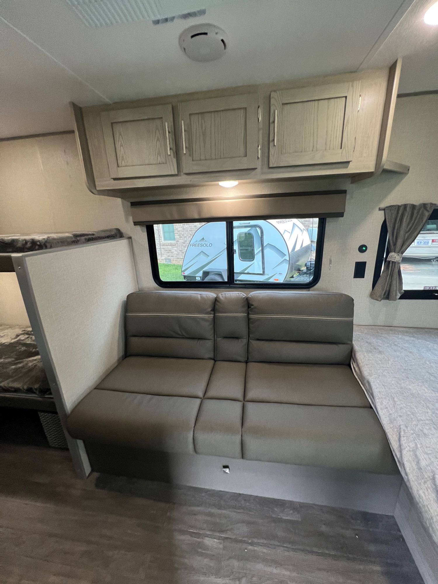 Cozy RV rental interior: gray dinette, bunk beds, and light wood cabinets. A window shows another RV outside.. Forest River Aurora 16 BHX 2023