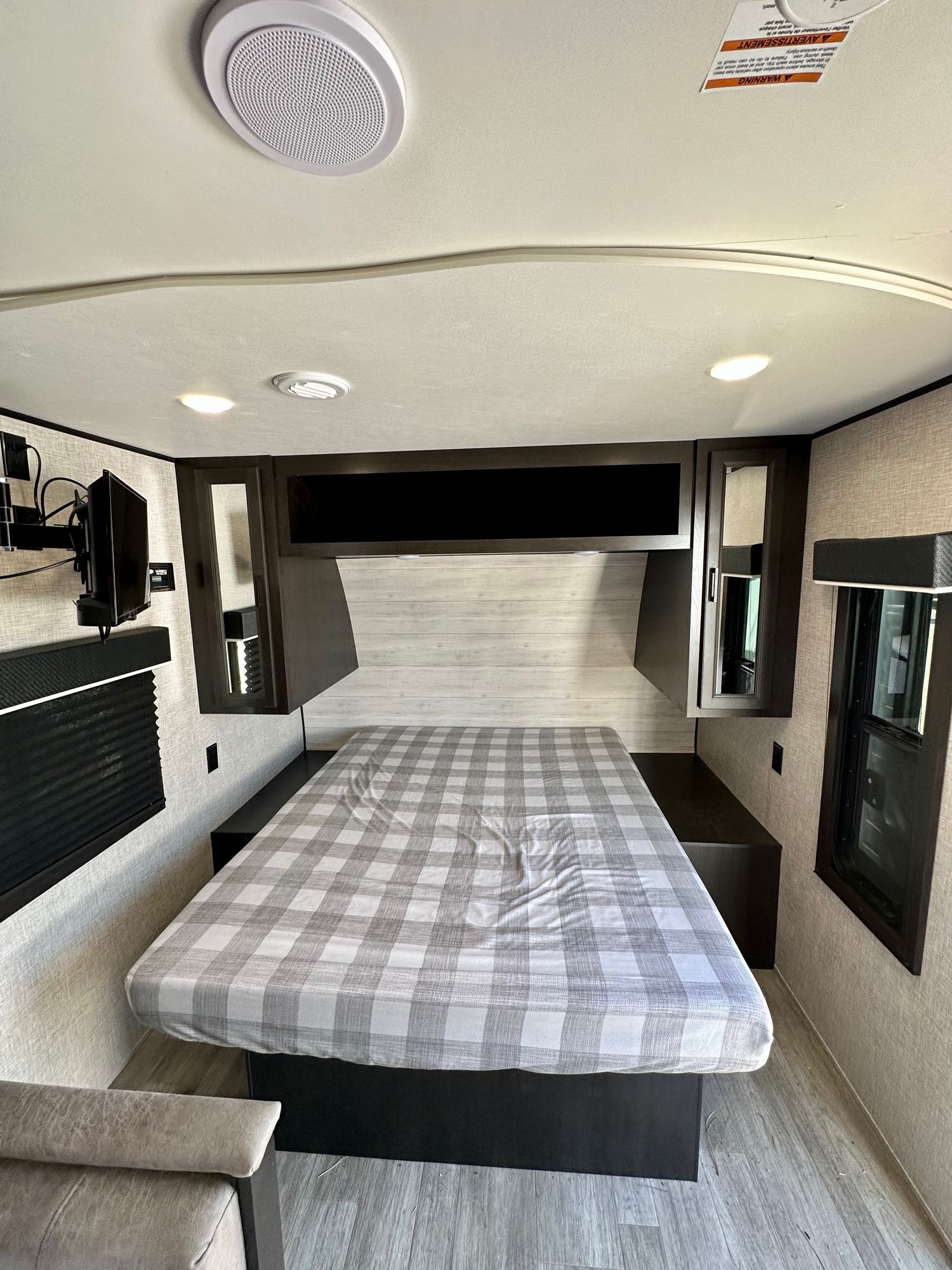RV rental interior: Cozy bedroom with plaid bed, overhead storage, TV, and windows. Perfect for road trips.. Jayco Jay Flight 2023