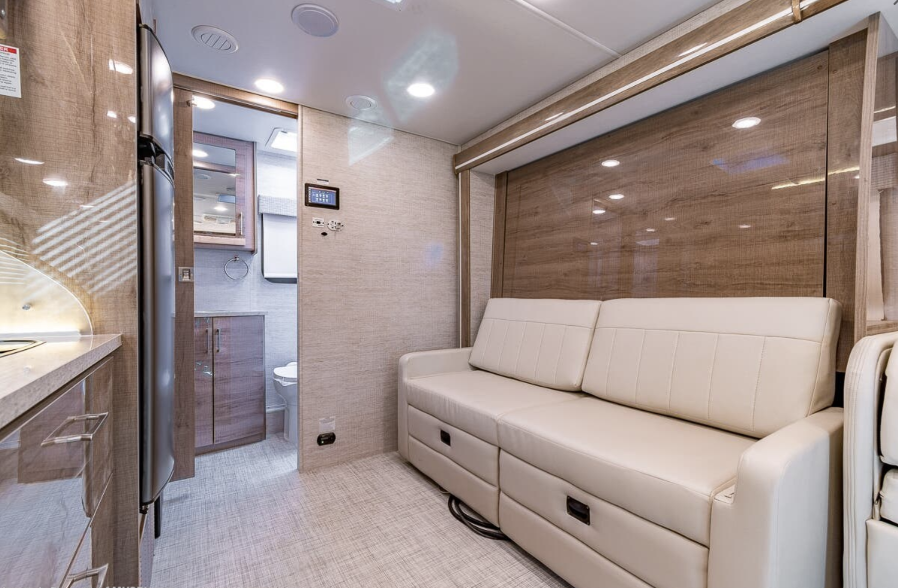 Spacious RV rental interior with cream sofa, modern kitchen area, and a glimpse of the bathroom. Ready for adventure.. Entegra Coach Qwest 2021