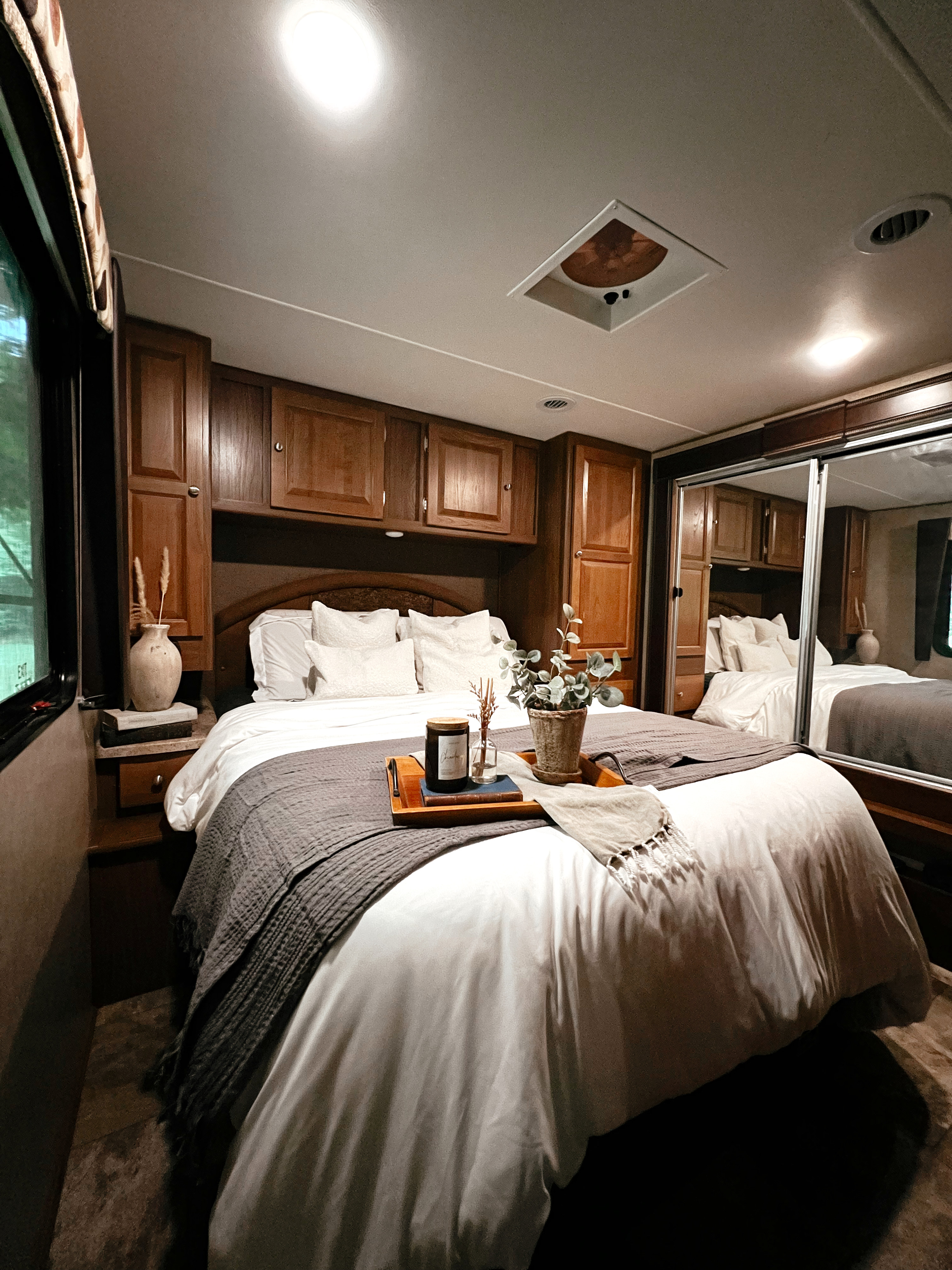Cozy RV rental bedroom: a comfy bed with decorative tray, rich wood cabinetry, and spacious mirrored closet.. Forest River Coachmen Leprechaun 2017