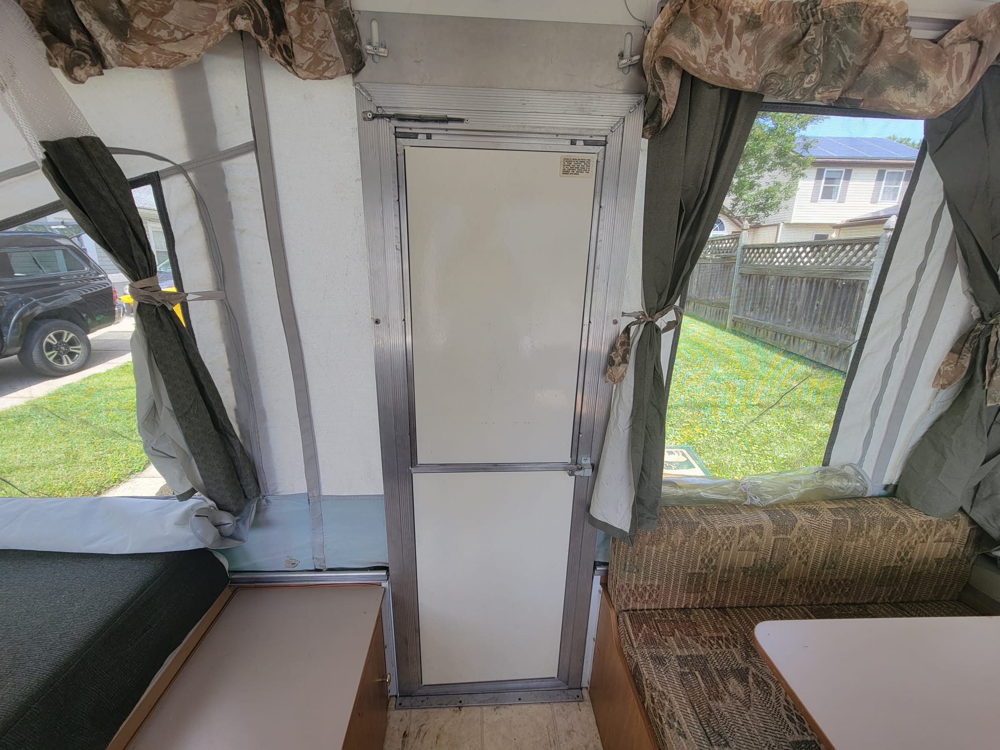 Interior of an rv rental pop-up camper, featuring a green mattress, patterned seating, and central door.. Coleman Taos 2003