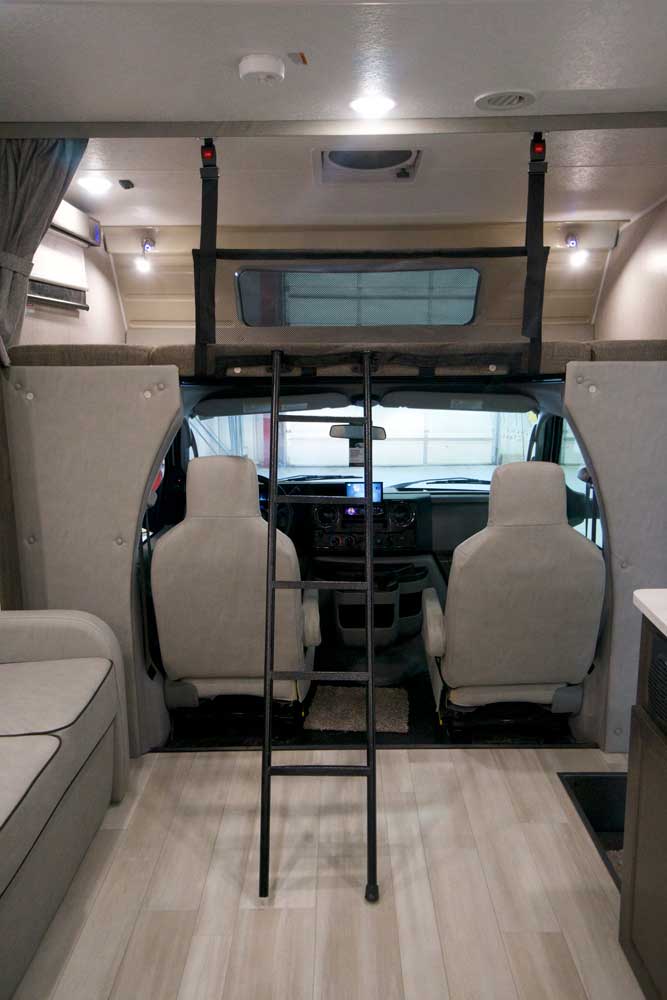 View inside an RV rental: over-cab bunk bed, ladder, cockpit, and living area with light flooring.. Coachmen Leprechaun 2022