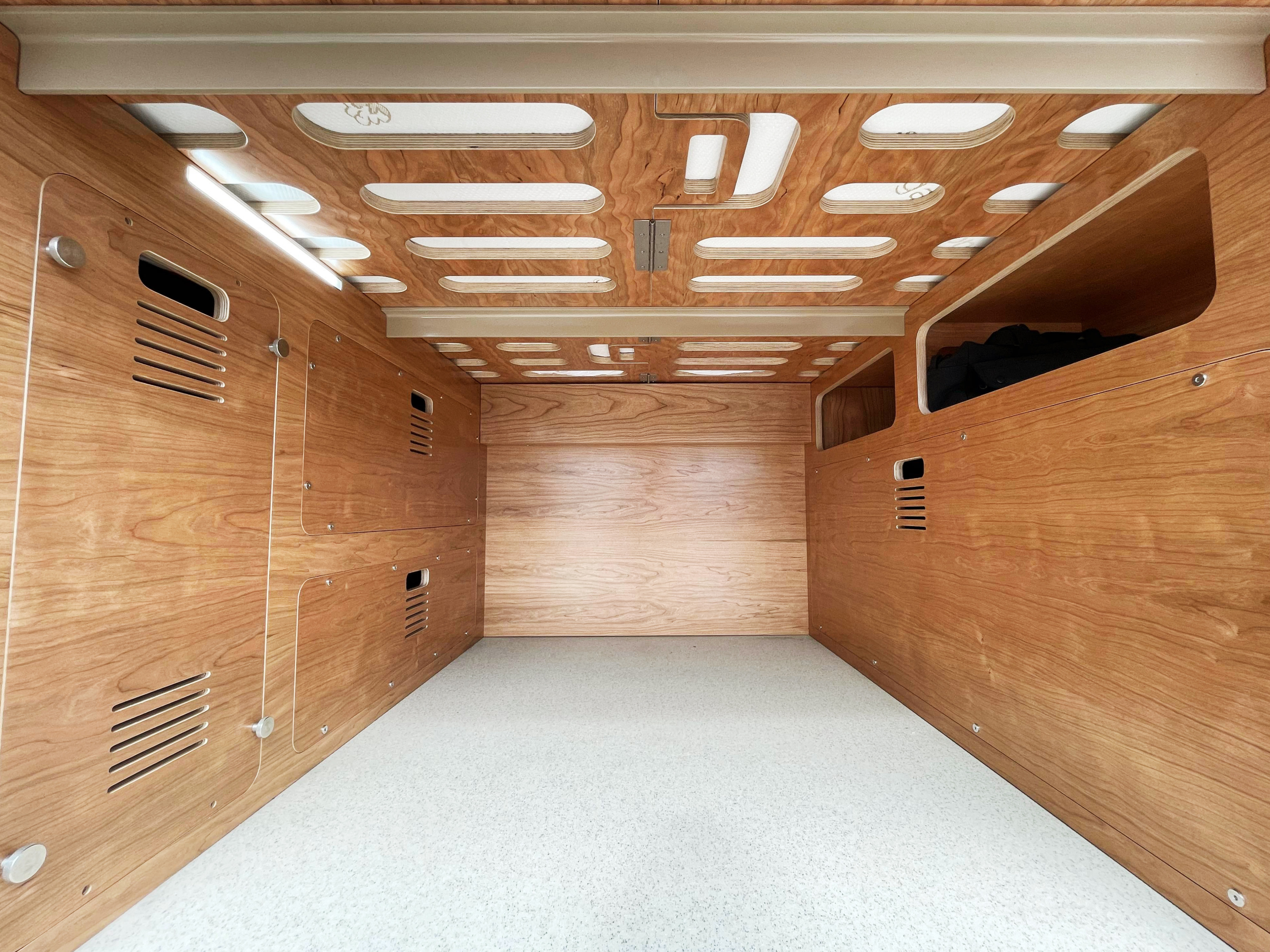 Inside a custom RV rental: wood-paneled interior, built-in storage, patterned ceiling with light strips, and a bright floor.. Mercedes-Benz Sprinter 2022