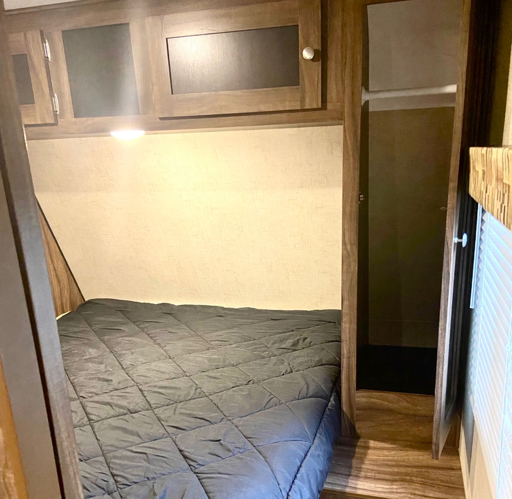 RV rental bedroom features a cozy bed with dark comforter, wood-look floor, overhead cabinets, and an open closet.. KZ Sportsman Showstopper S280BHSS 2017