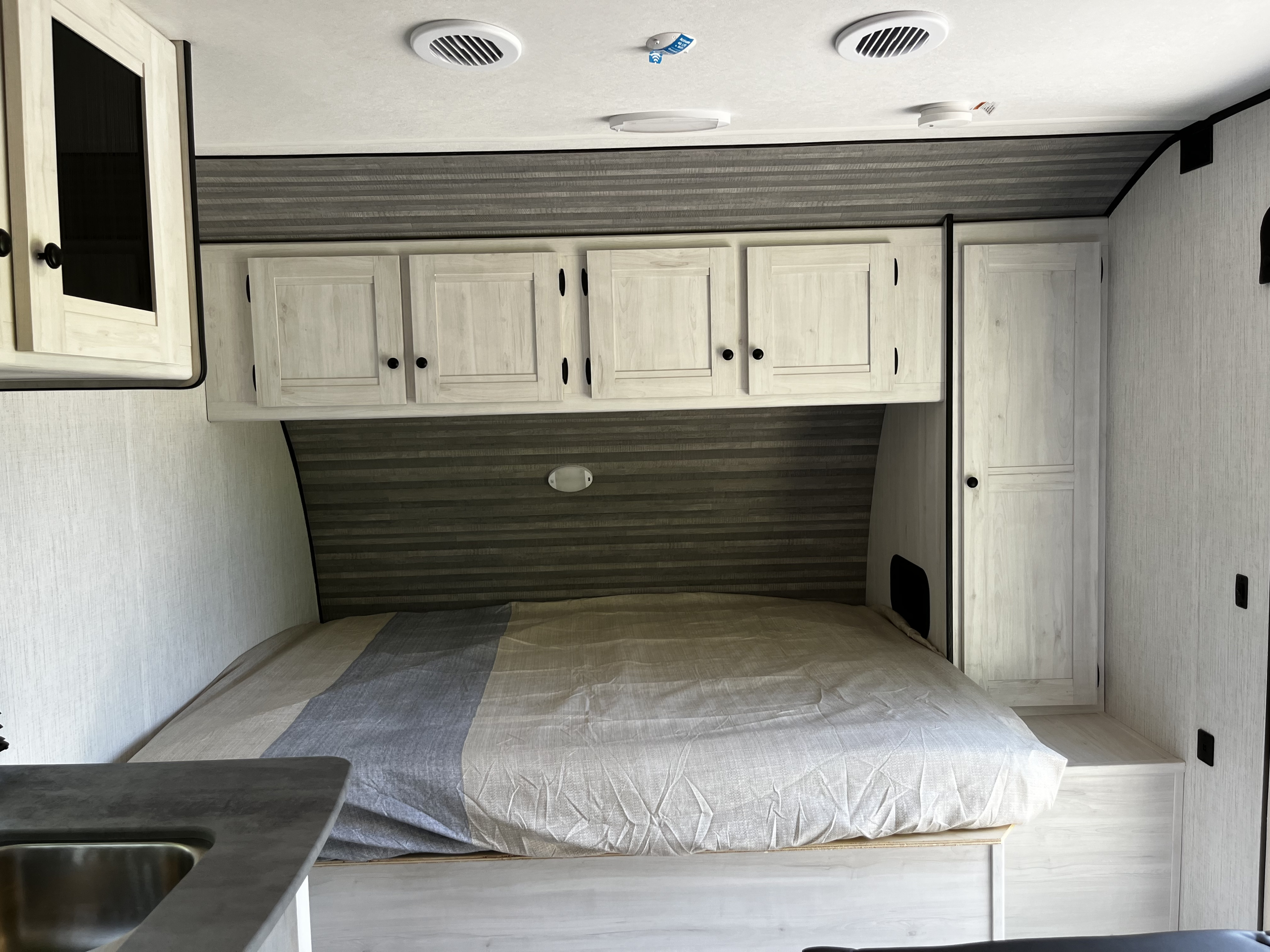 Cozy RV rental bedroom featuring a bed, overhead cabinets, wardrobe, and ceiling vents.. Heartland RVs Trail Runner 2023