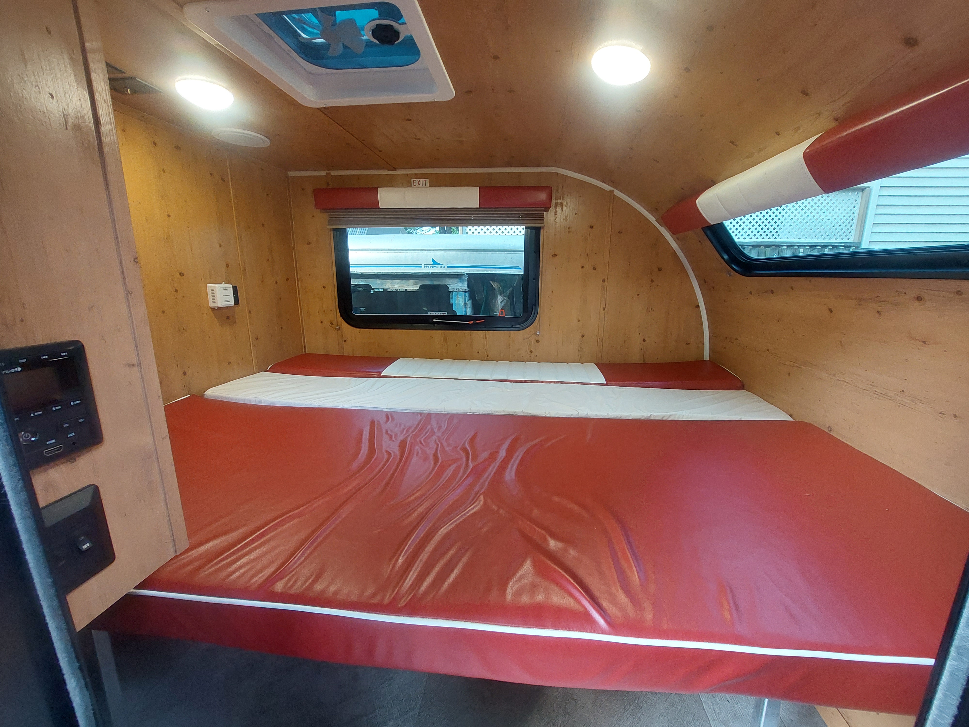 Cozy RV rental interior: wood-paneled sleeping area with red and white bed, window, and overhead lighting.. Sunset Park RV SunRay 2022