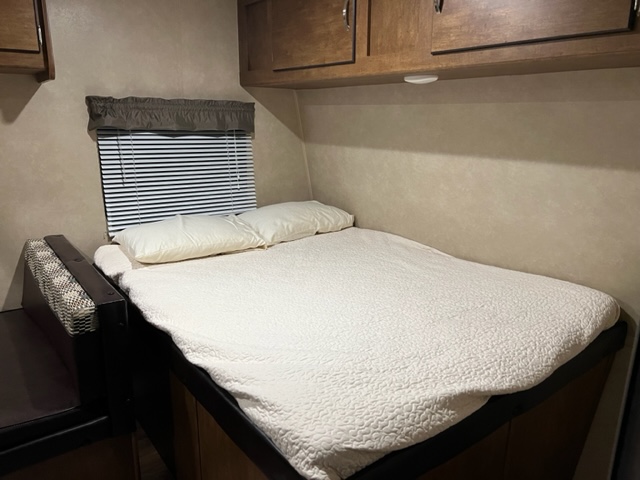 Cozy rv rental bedroom showing a comfortable bed, window with blinds, and overhead cabinets.. Forest River Wildwood 2017
