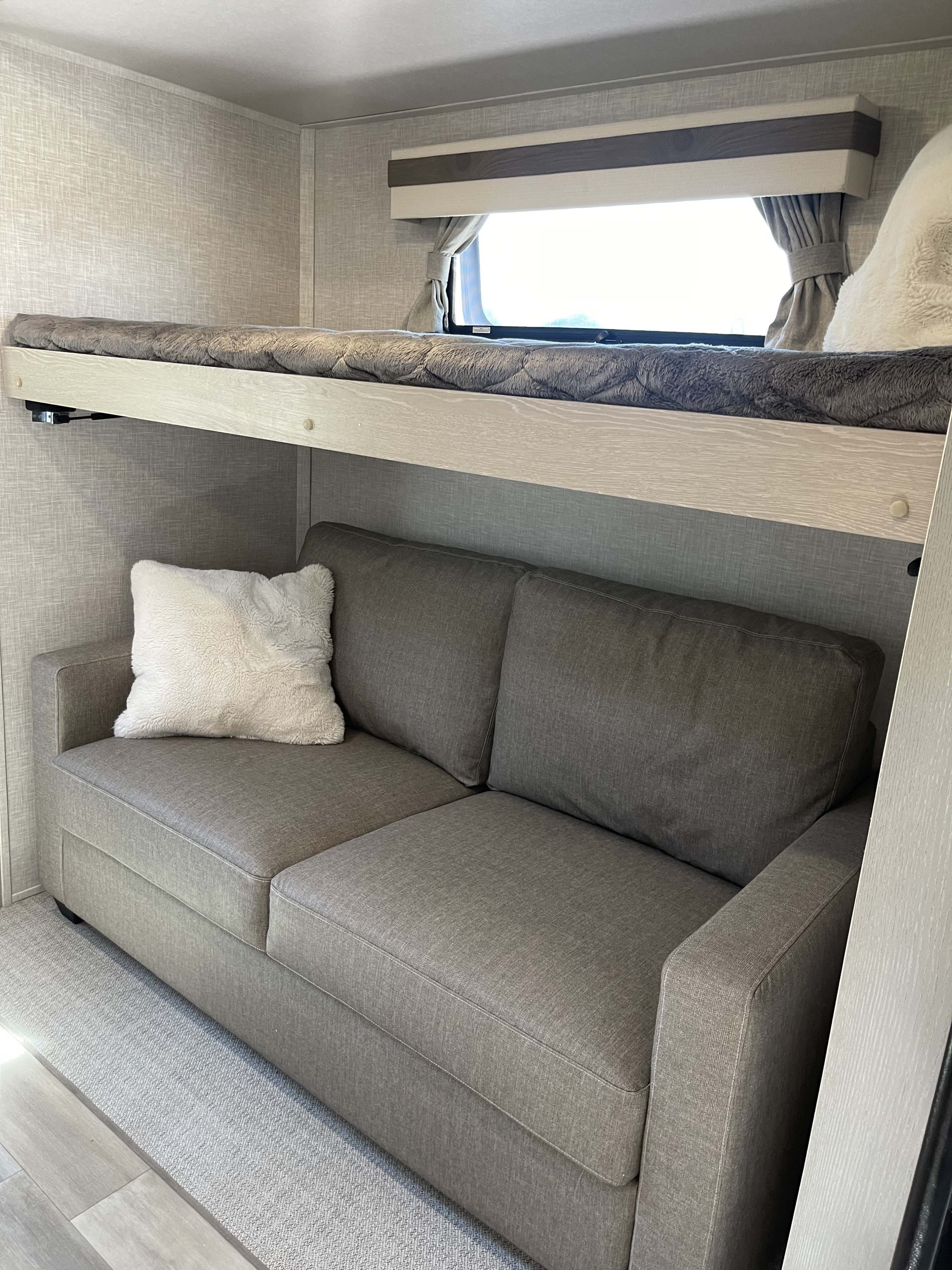 Cozy RV rental interior with a comfy gray sofa below a top bunk bed, offering a practical sleeping and living area.. Forest River Rockwood Signature 2023