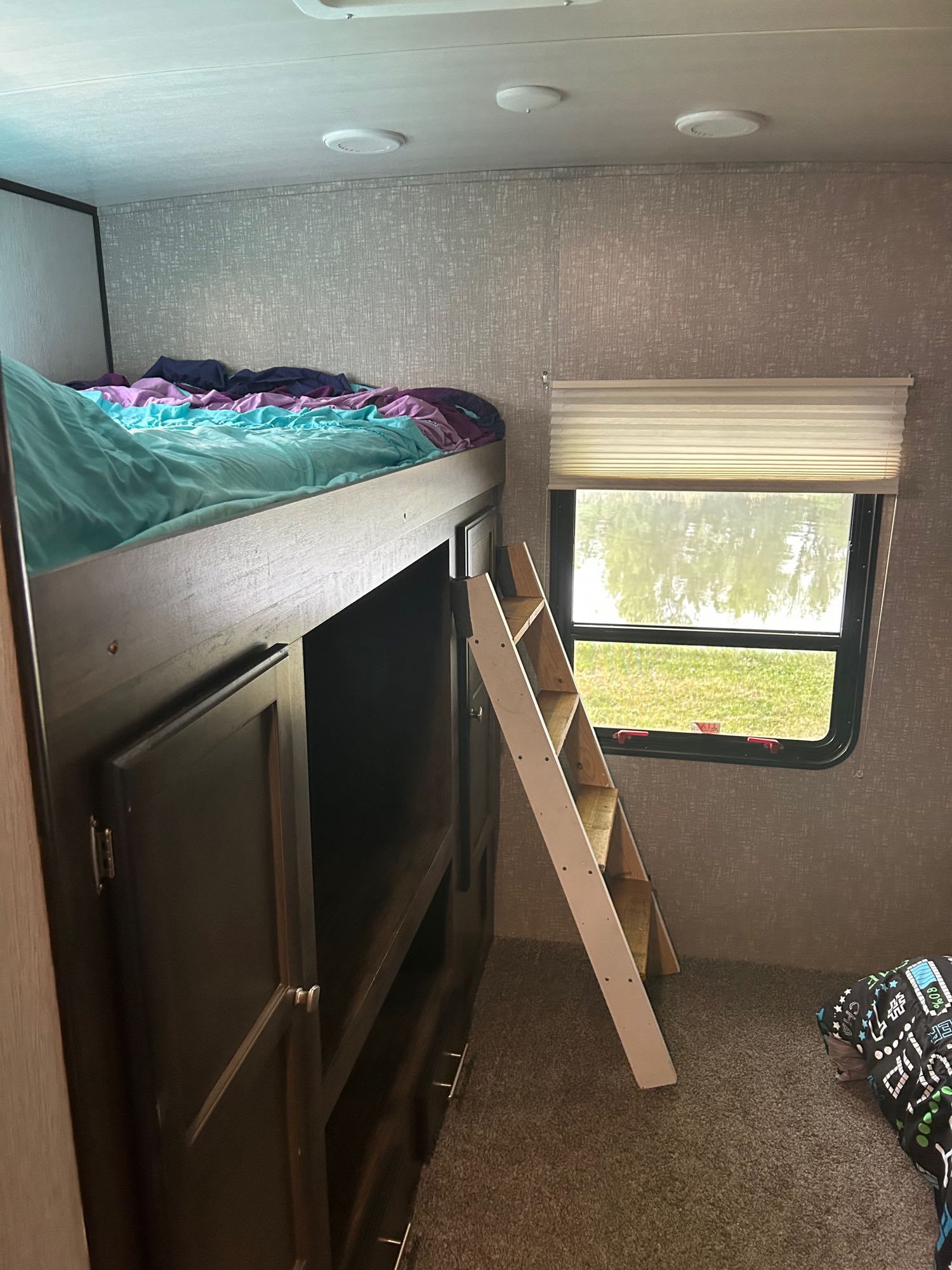 Cozy RV rental interior: a top bunk bed with colorful bedding, a wooden ladder, and a window revealing an outdoor scene.. Heartland RVs Mallard 2020