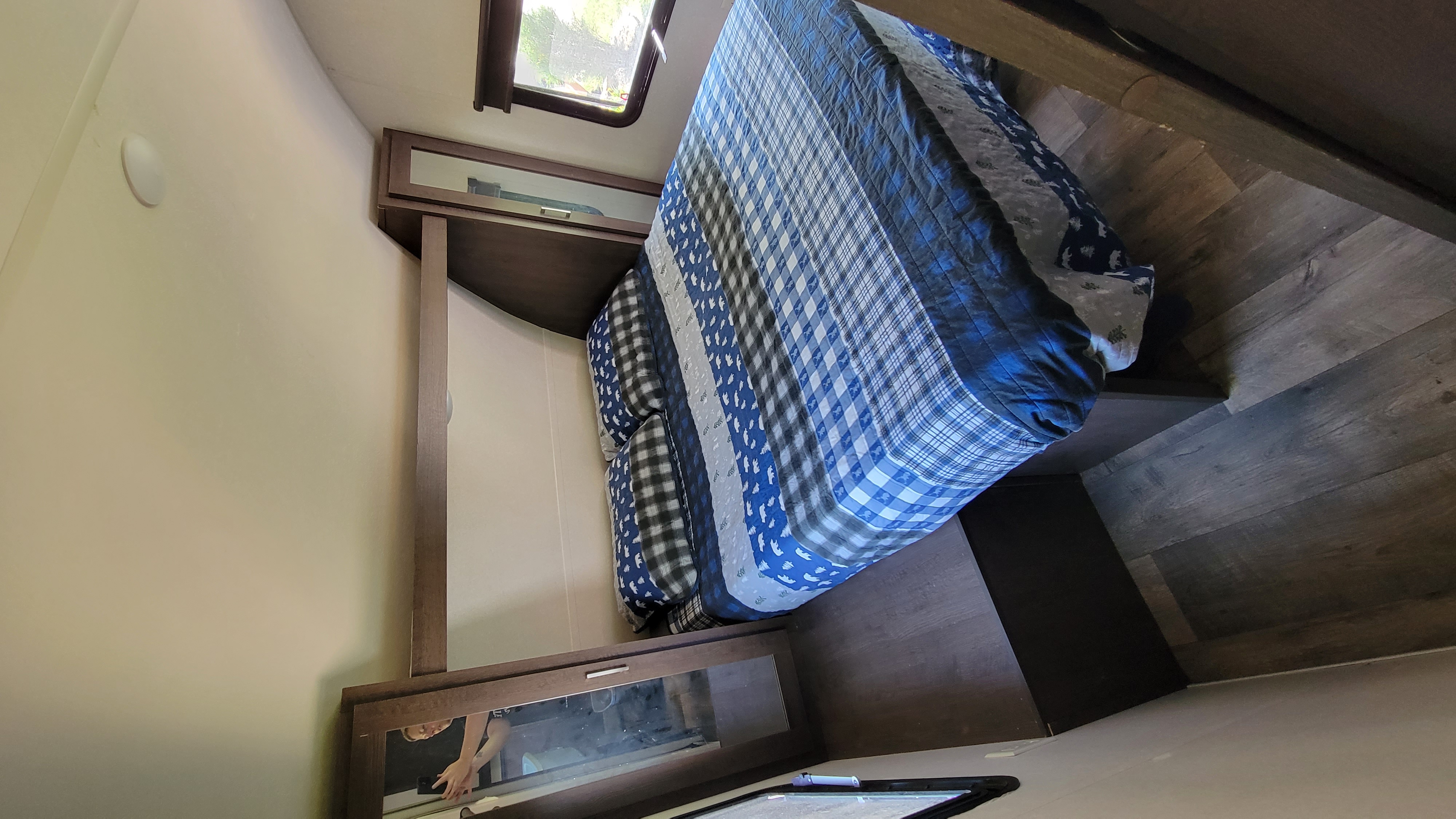 Bright RV rental bedroom showing a bed with blue and white comforter, modern overhead cabinets, and a window for natural light.. Forest River Salem Cruise Lite 2018