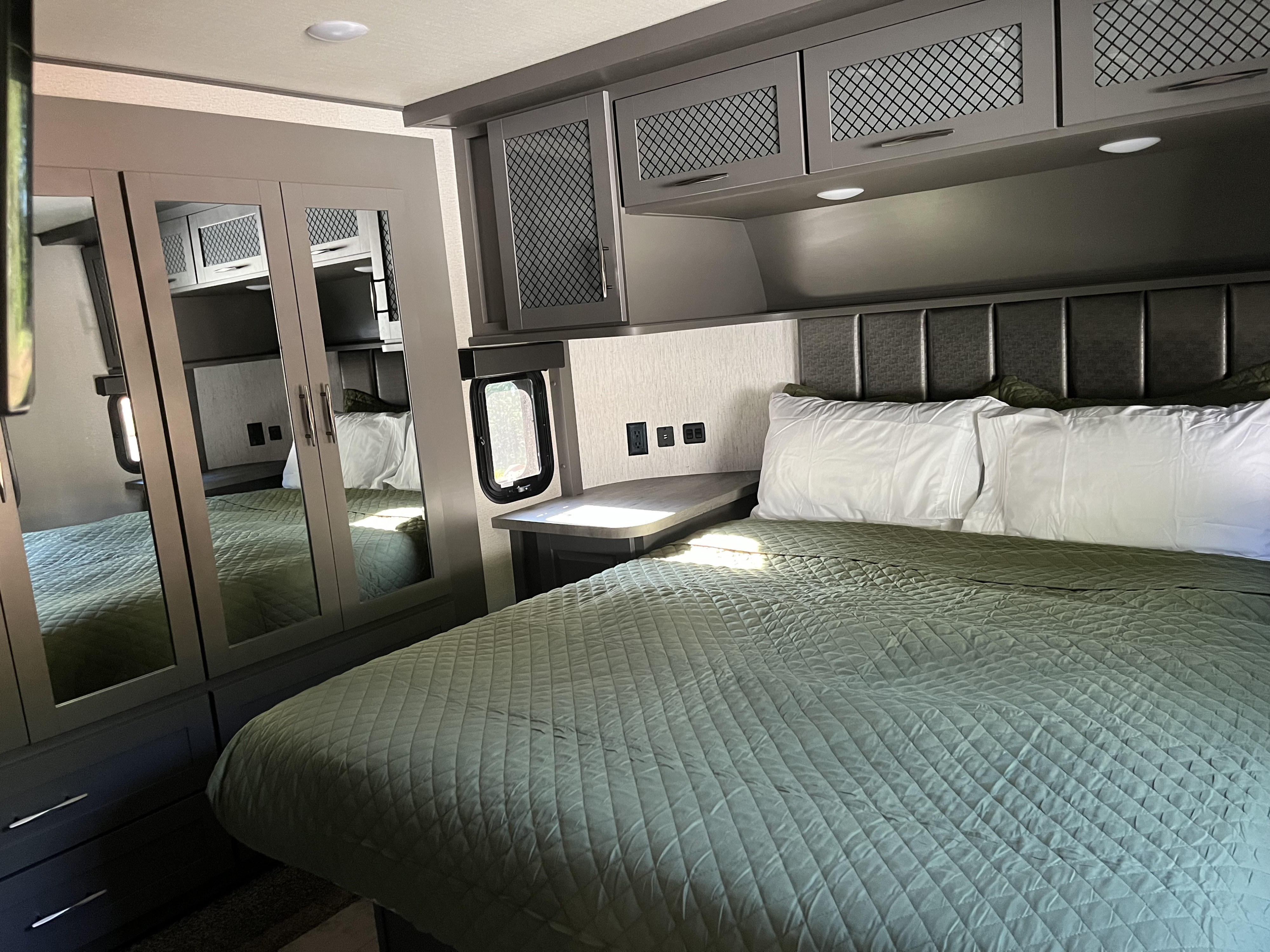 Spacious and modern RV rental bedroom with comfortable bed, ample storage, and bedside charging for your travels.. Grand Design Momentum 2021