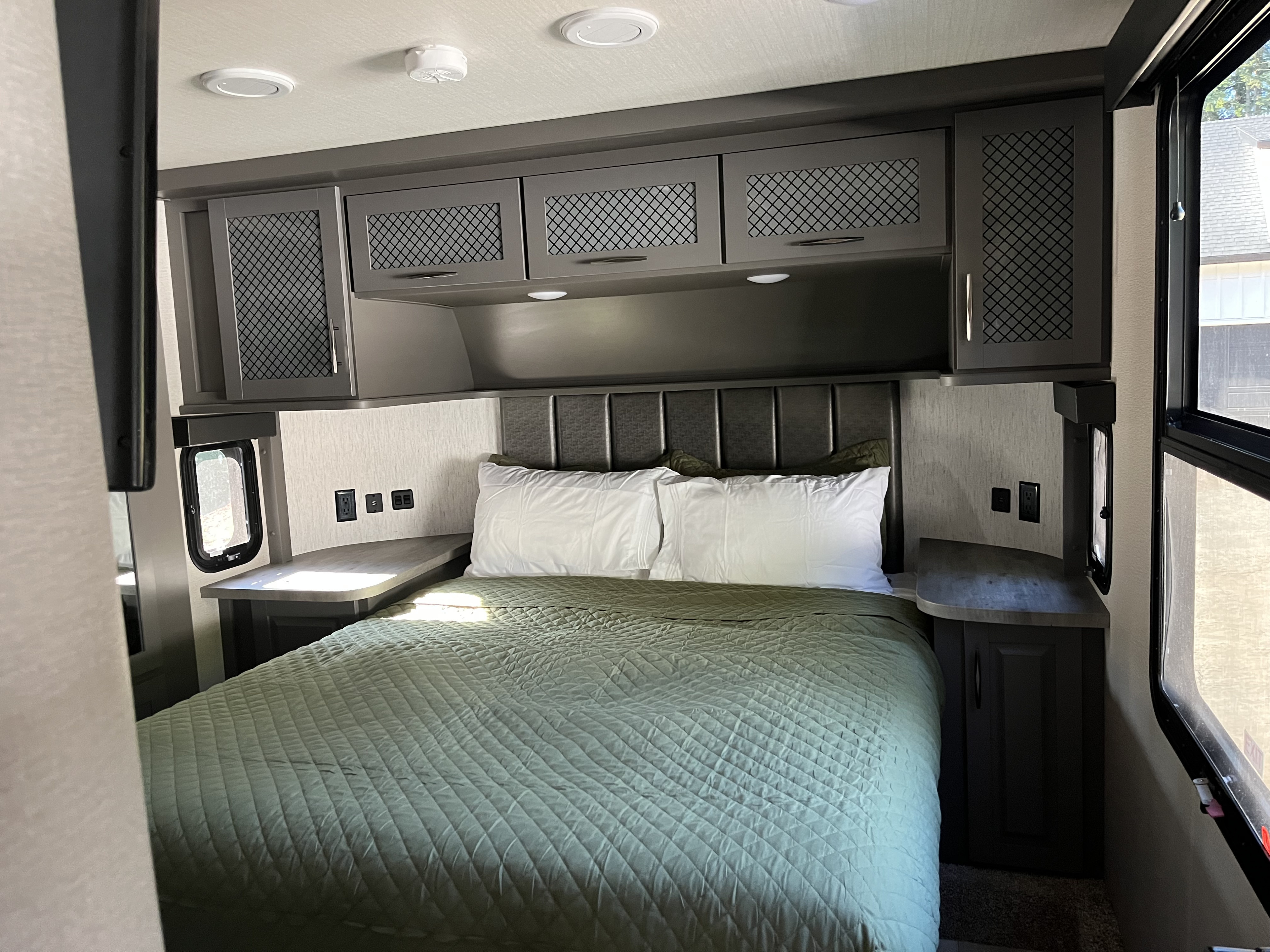 Comfortable RV rental bedroom featuring a queen bed with padded headboard, overhead storage, and bedside outlets.. Grand Design Momentum 2021