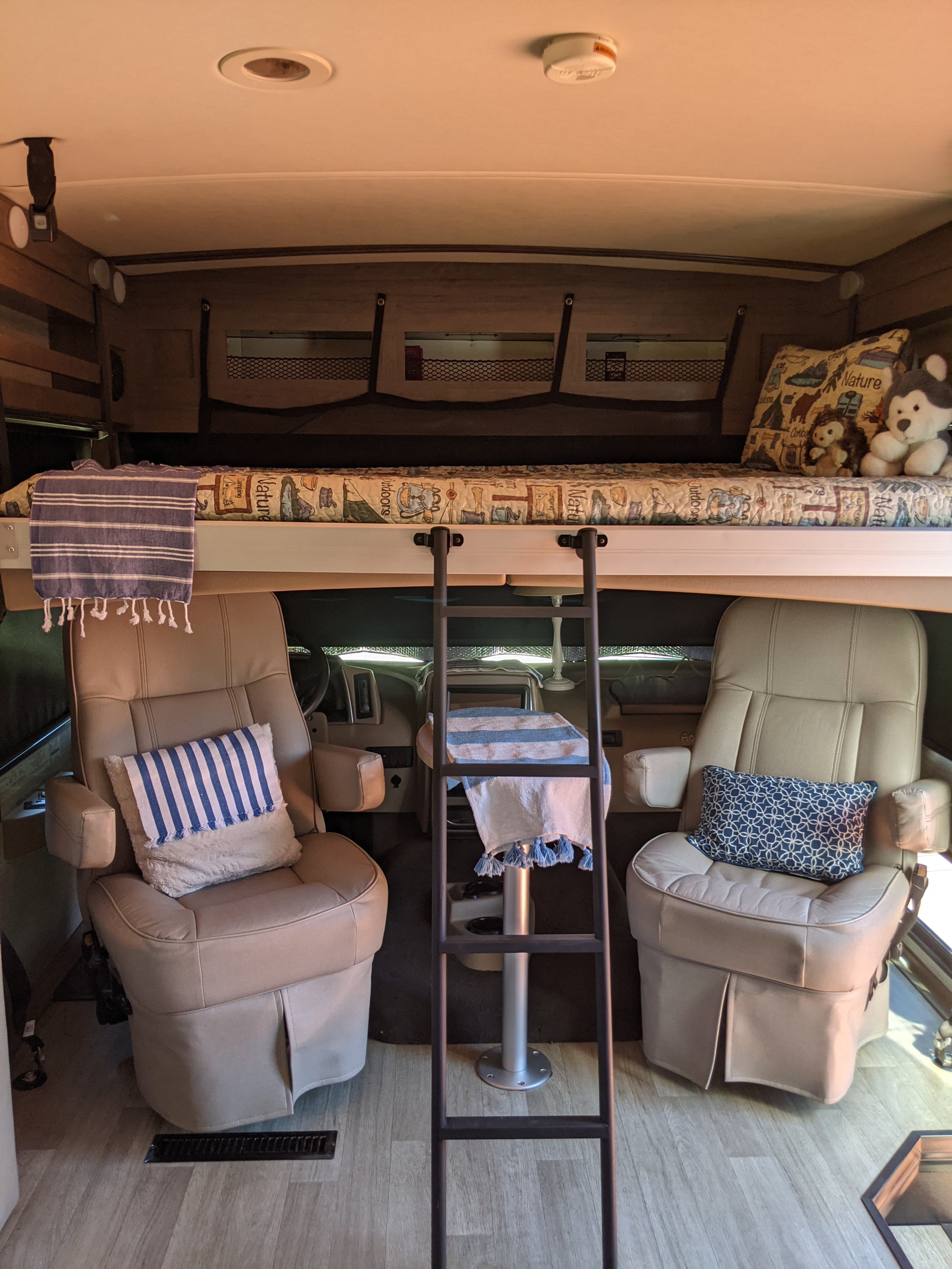 An RV rental's inviting interior shows a bunk bed over the cab, ladder access, and plush captain's chairs.. Winnebago Adventurer 2021