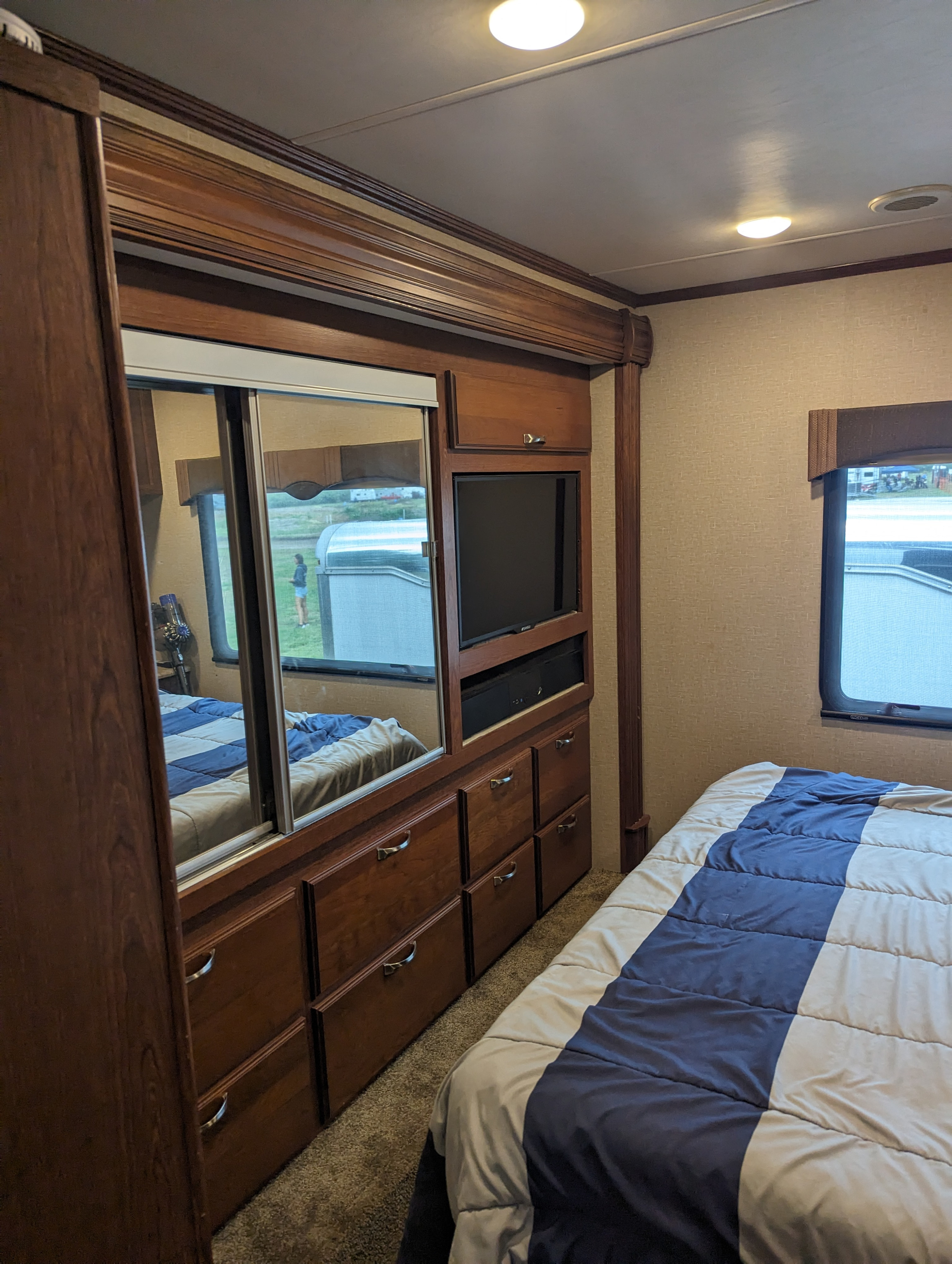 RV rental bedroom interior featuring a comfortable bed, mirrored closet, TV, and built-in storage drawers.. Dynamax Force 2015