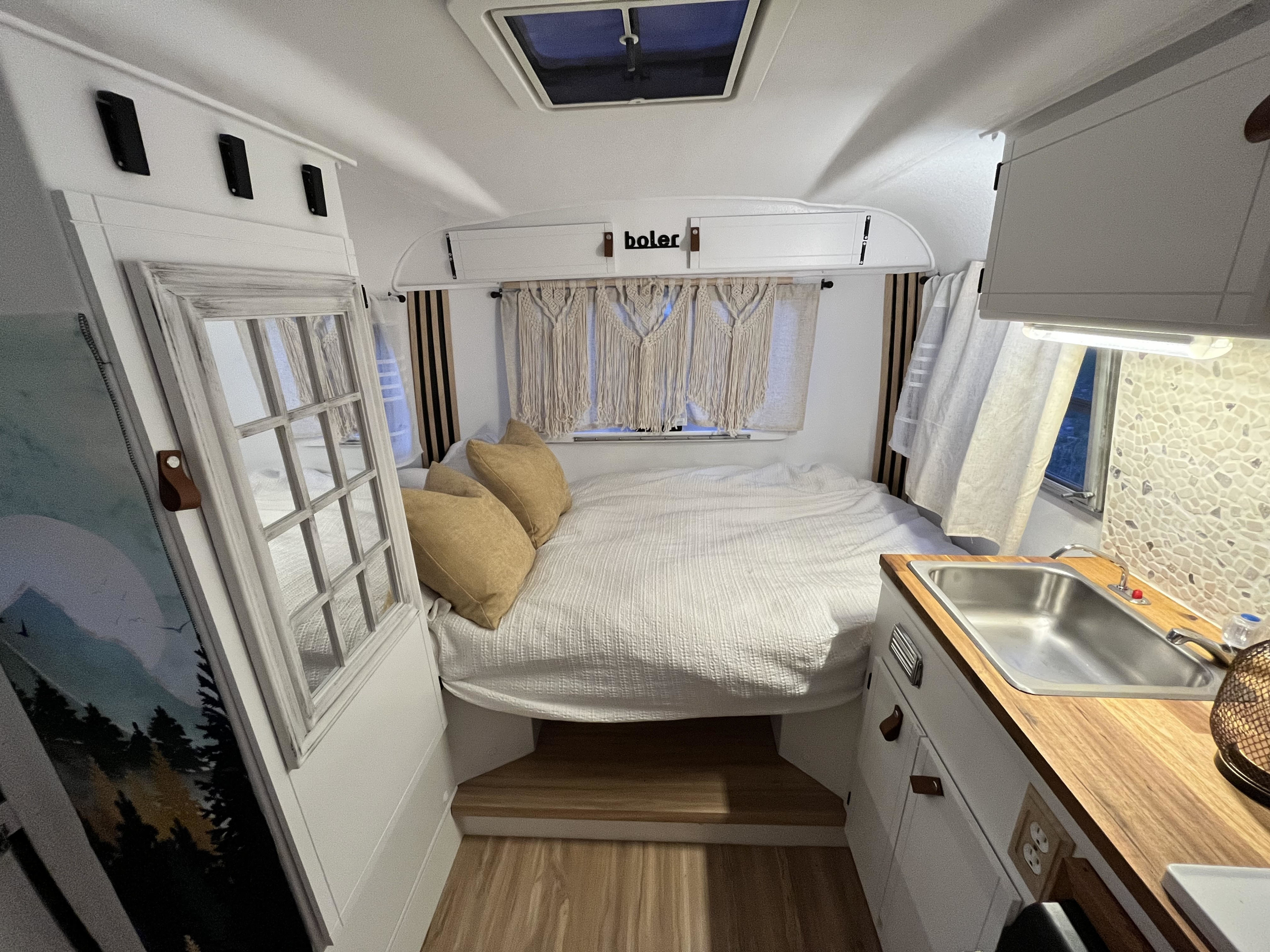 View inside a white Boler RV rental: cozy bed, compact kitchen with sink, and bright, modern interior.. Boler 1300 1978