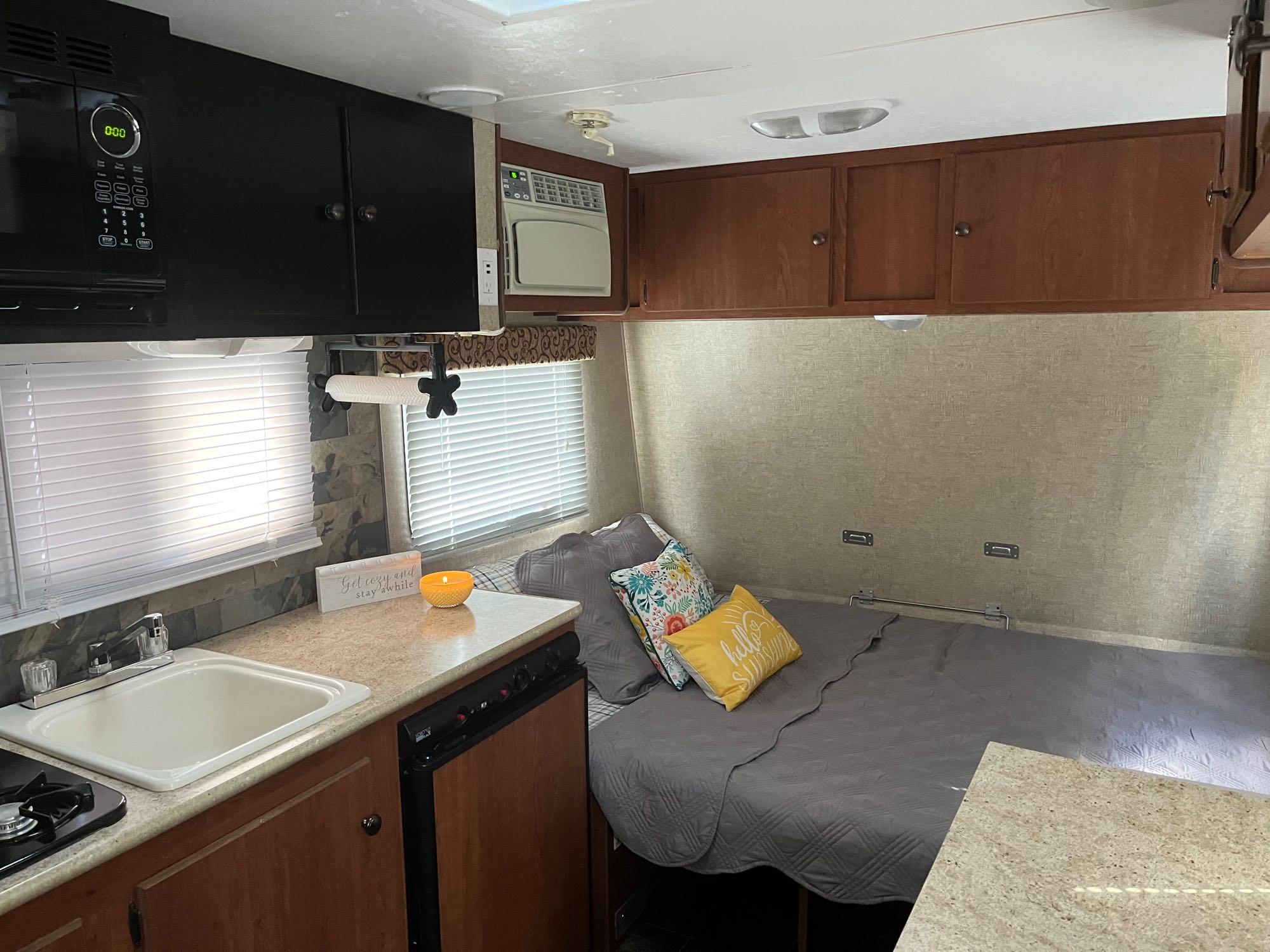 RV rental interior: compact kitchen (sink, stove, microwave), cozy bed with pillows, and overhead AC unit. Ideal for camping.. Sportsmen KZ 2014
