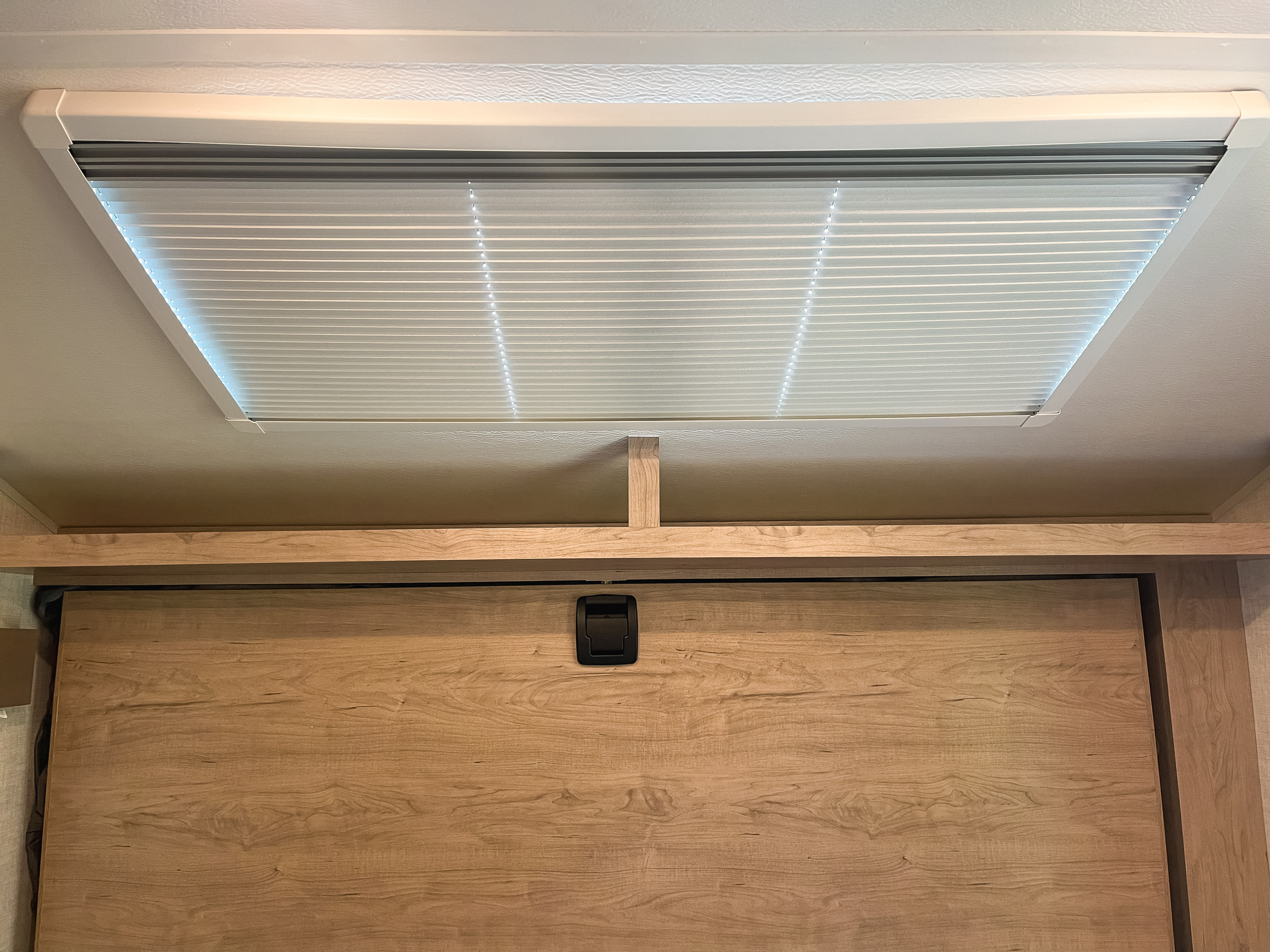 Interior of an RV rental, featuring a pleated ceiling light or skylight and a light wood cabinet with a black latch.. Ember Overland 2022