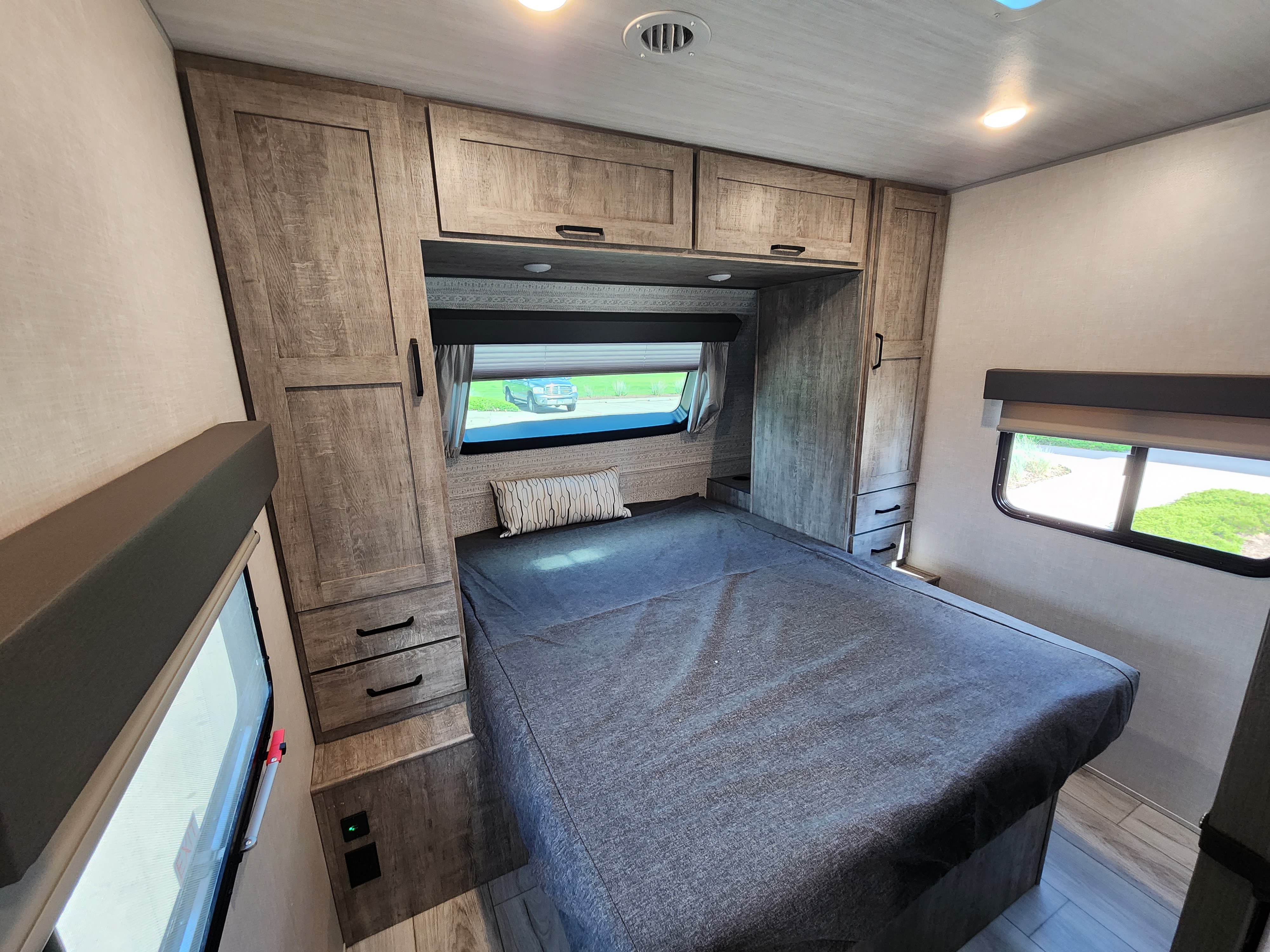 This RV rental features a comfortable bedroom with overhead cabinets, wardrobes, and a window to enjoy the view.. Forest River Grand Surveyor 267RBSS 2023