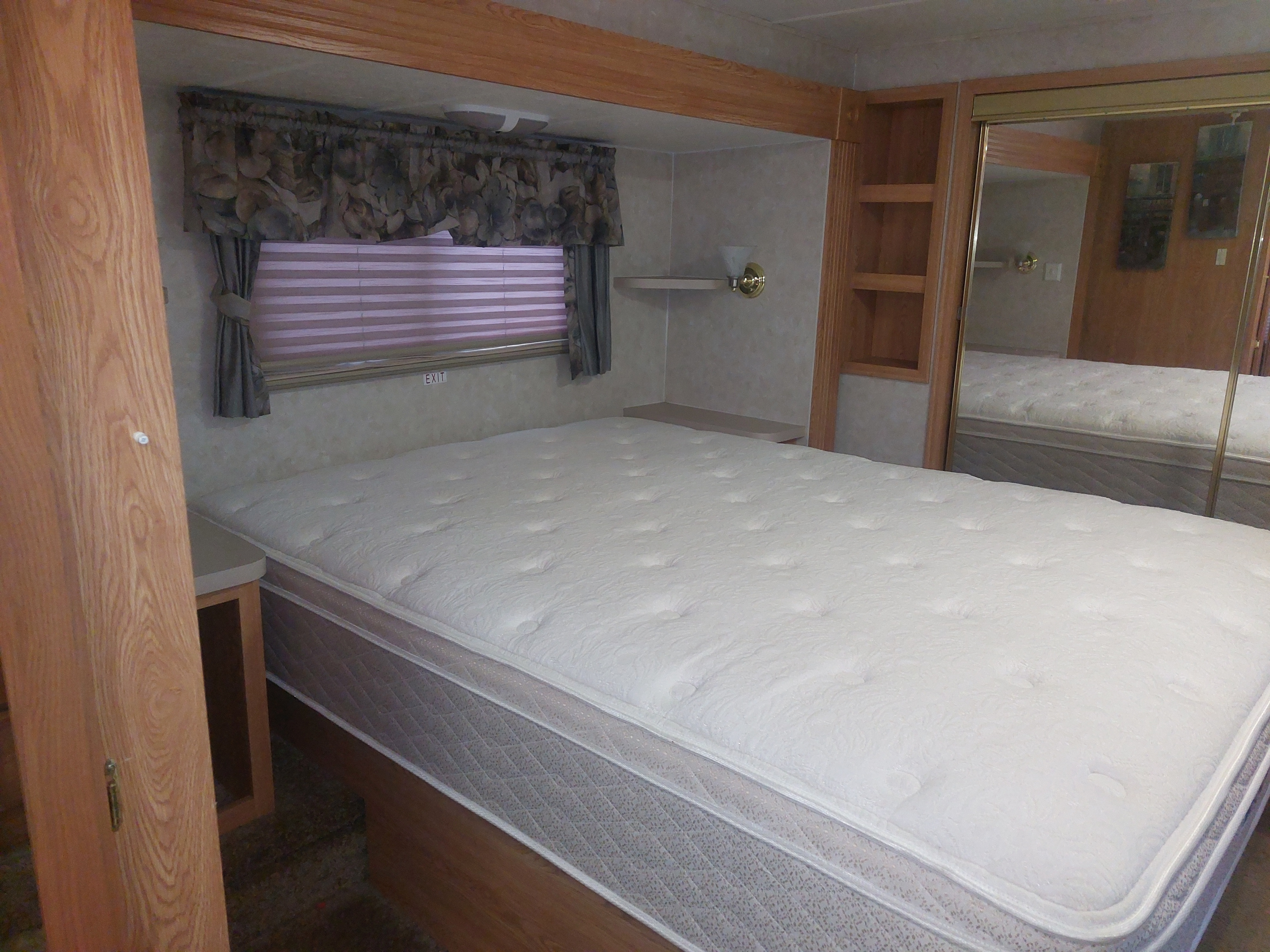 Comfortable RV rental bedroom with a large mattress, window, and mirrored closet, highlighted by an 'EXIT' sign.. Crossroads Silverado 2005