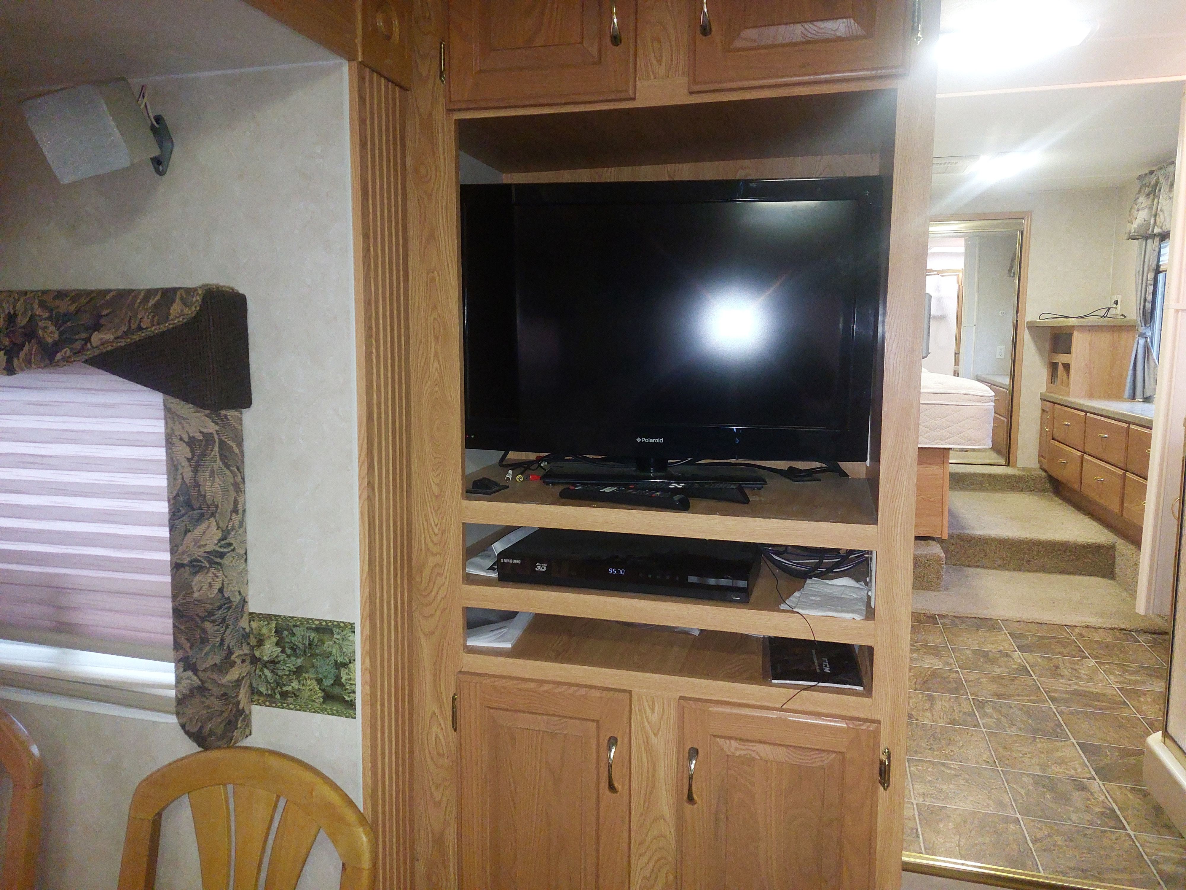 Inside an RV rental: a wooden entertainment center with TV, window blinds, and steps leading to the bedroom area.. Crossroads Silverado 2005