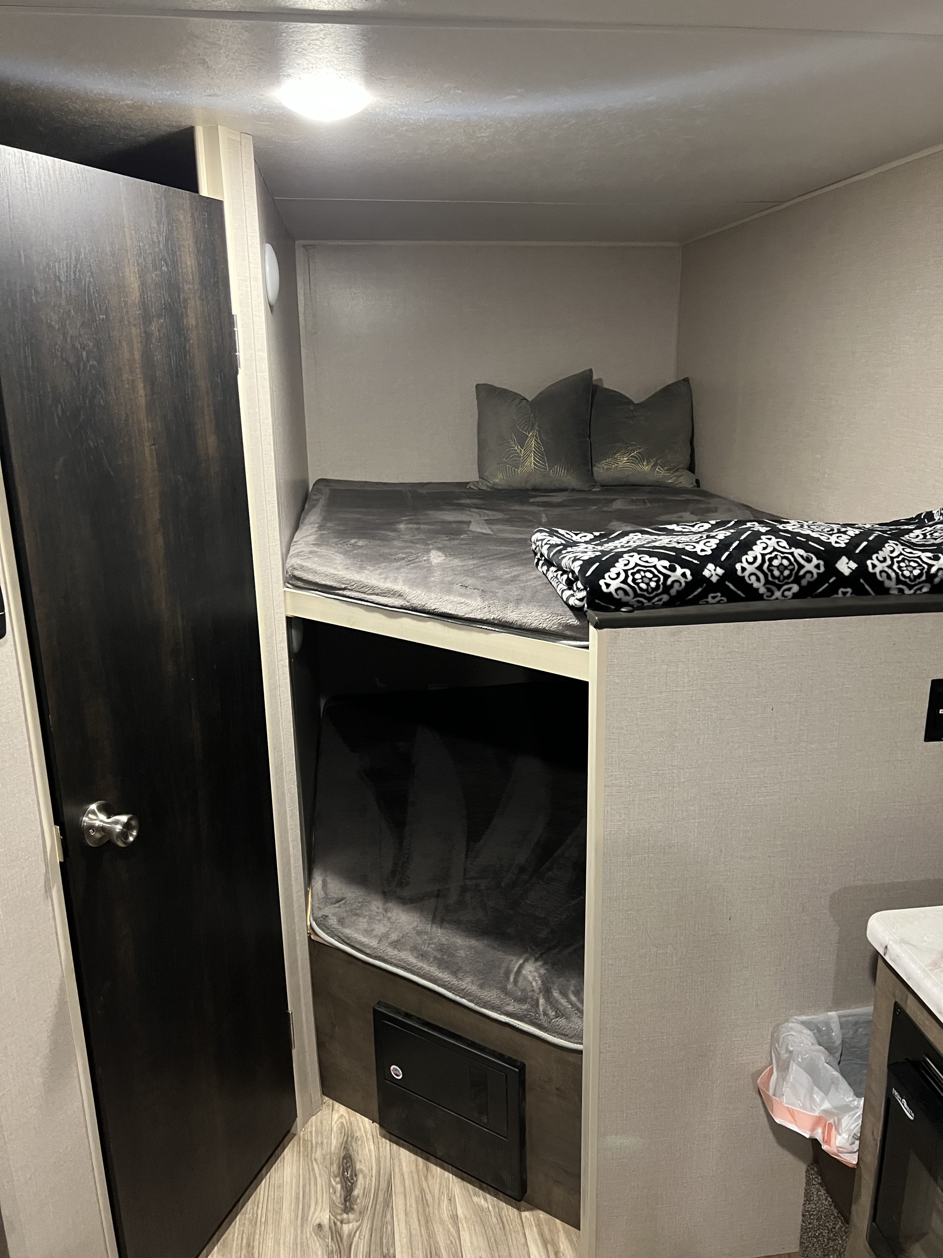 A compact, cozy RV rental interior featuring two bunk beds with bedding, a nearby door, and a fuse box.. K-Z Manufacturing Escape 2020