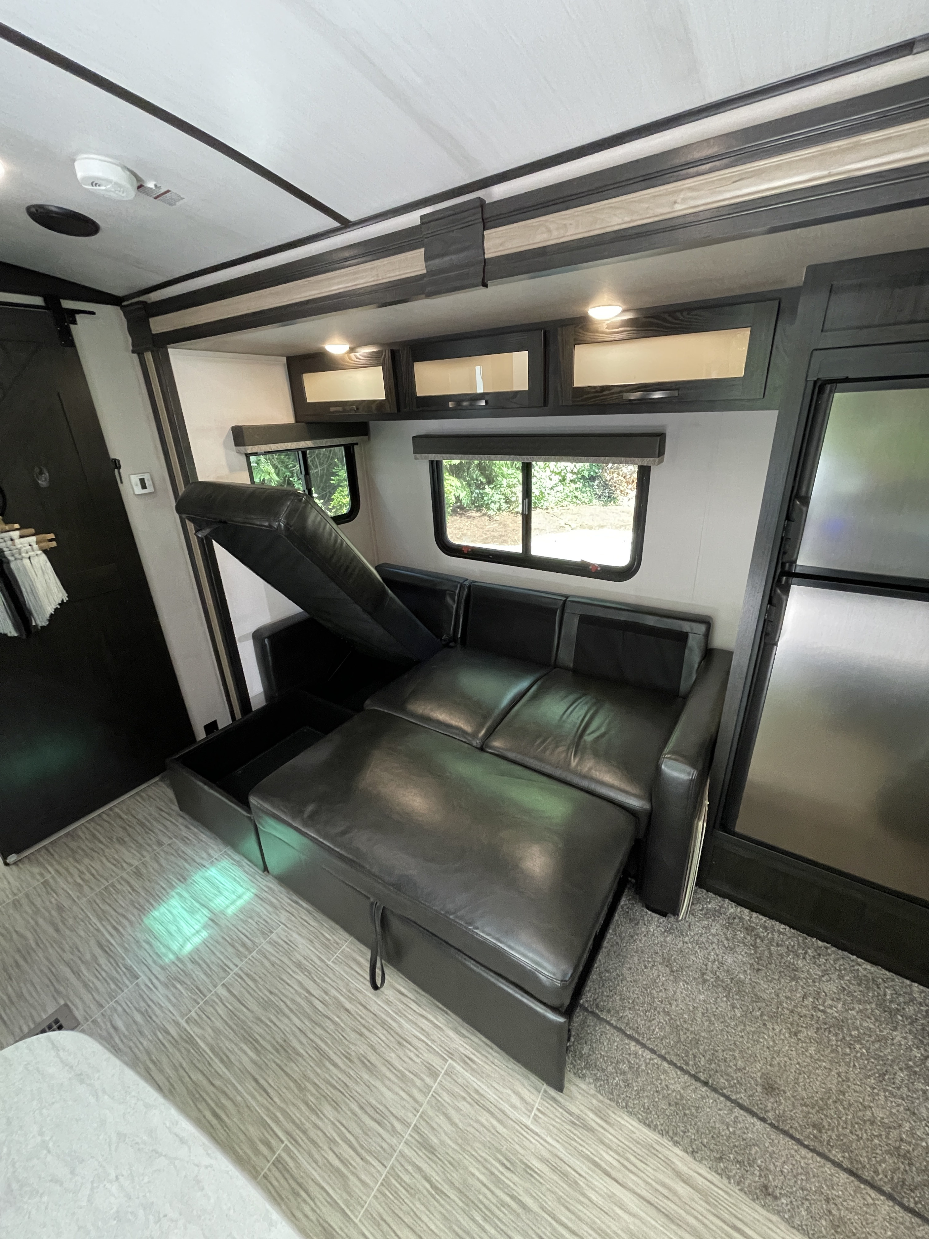 RV rental living area featuring a pull-out sofa bed, overhead cabinets, windows, & fridge. Great for travel!. Forest River Surveyor Luxury 2020