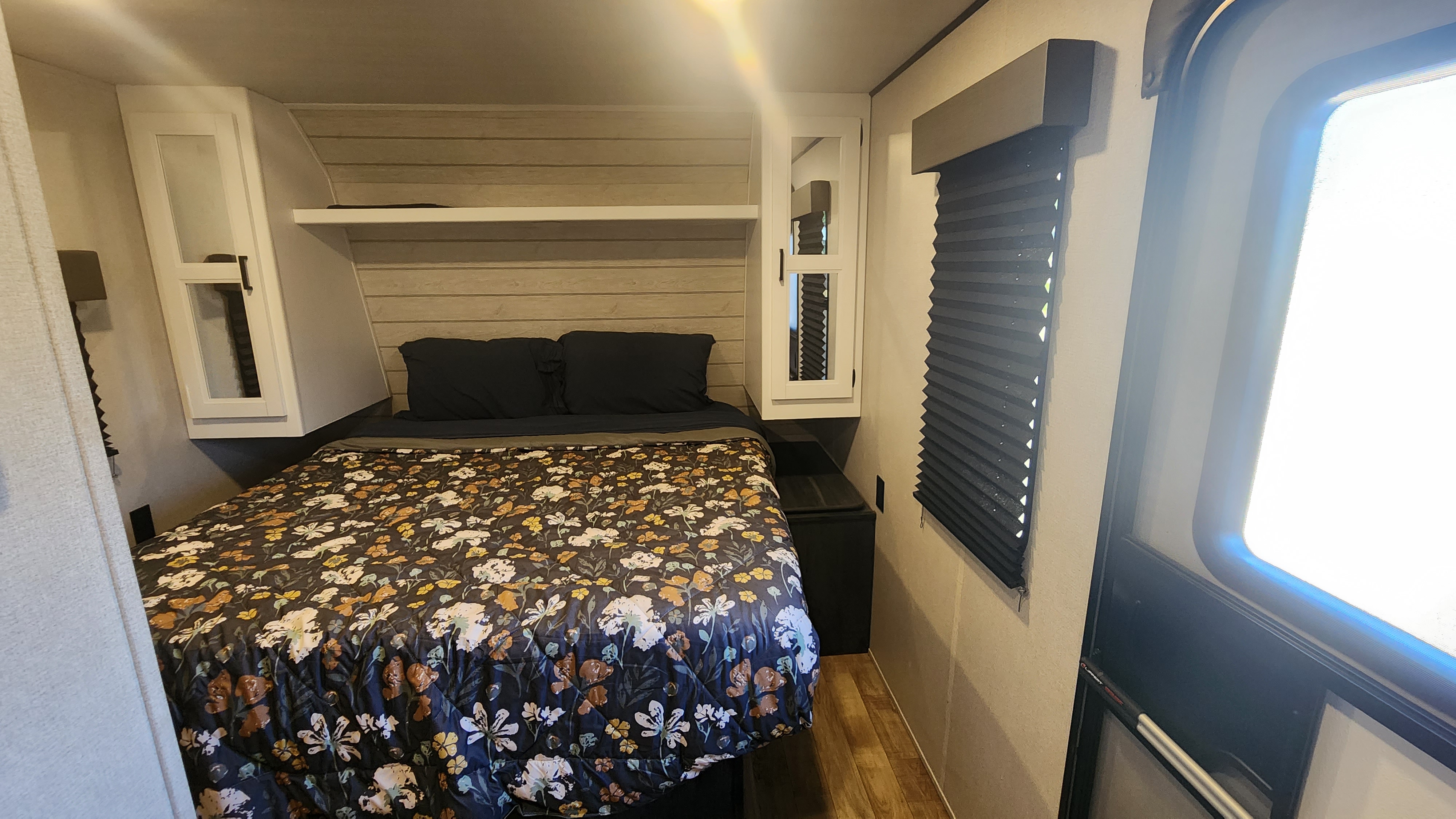 Inside an RV rental: a compact bedroom featuring a floral bed, overhead storage, and a window with privacy blinds.. Hideout Hideout 2022