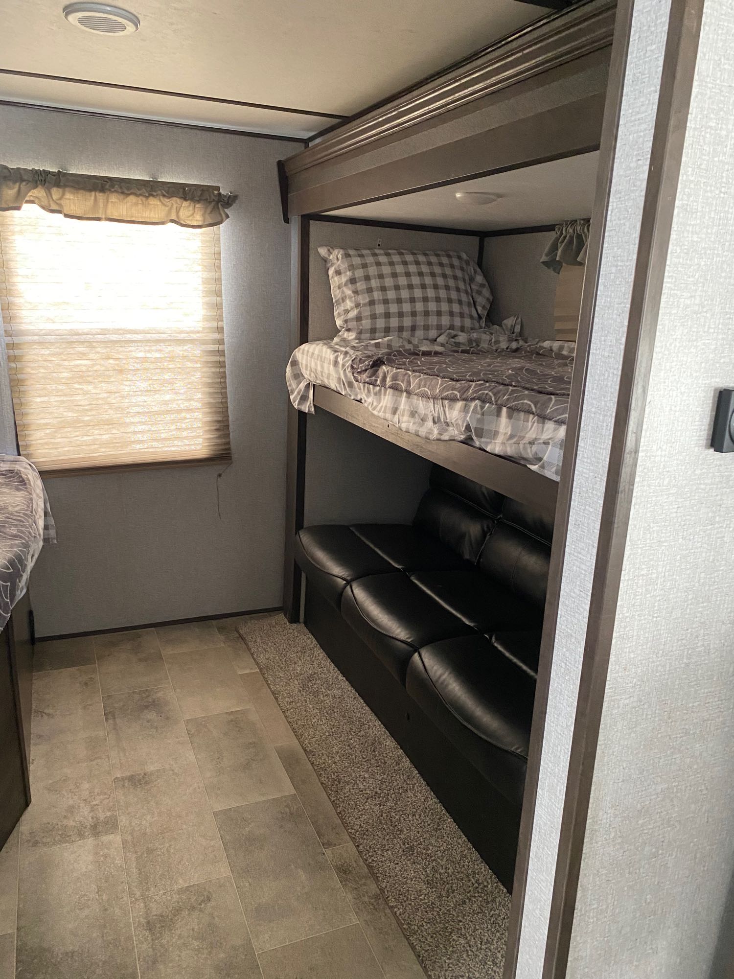 RV rental interior featuring bunk beds over a black sofa. A bright window illuminates the cozy sleeping & lounge area.. Dutchmen Coleman Lantern 2020