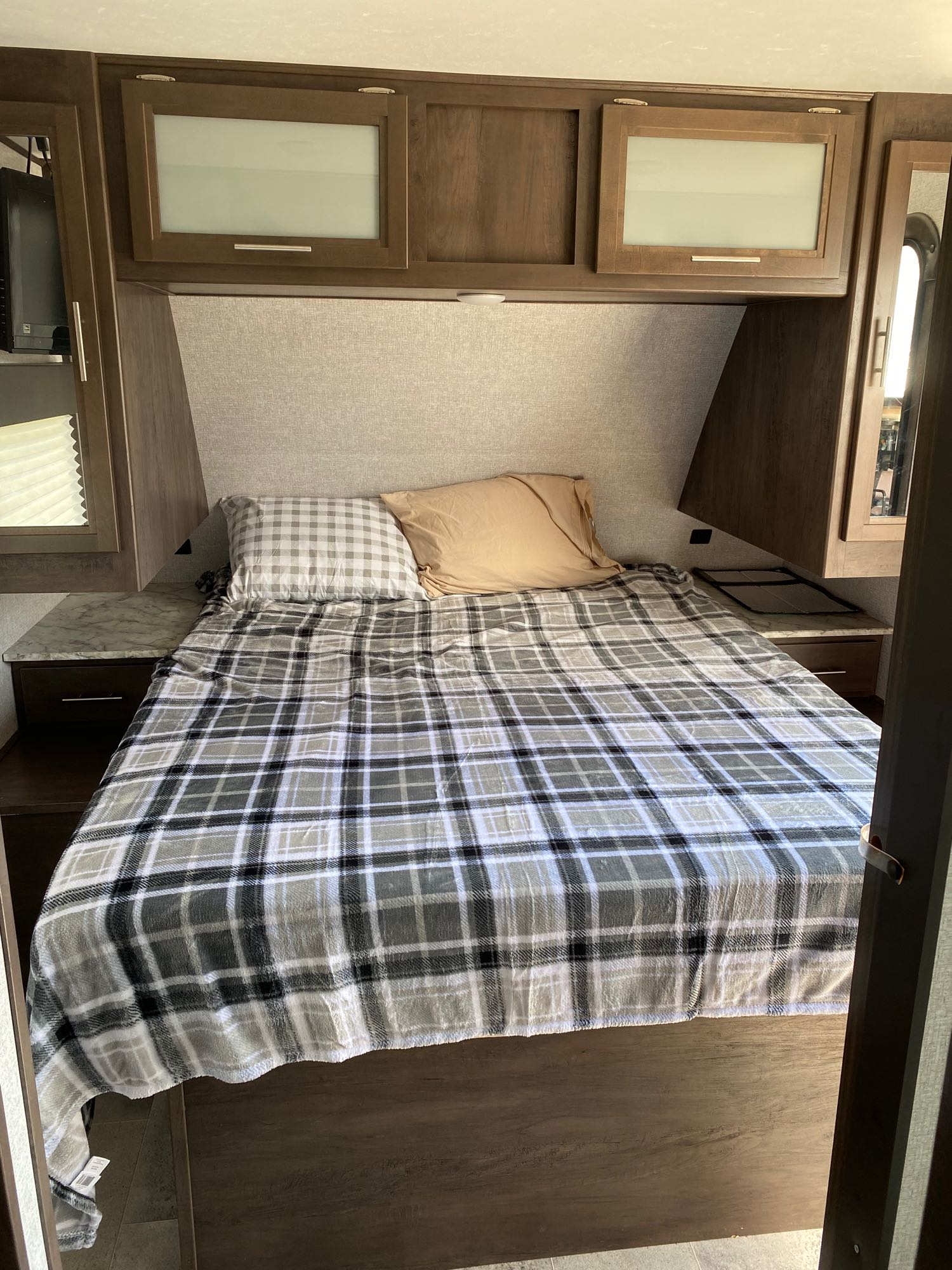 Cozy RV rental bedroom interior featuring a plaid-covered bed, overhead storage cabinets, and side tables with drawers.. Dutchmen Coleman Lantern 2020