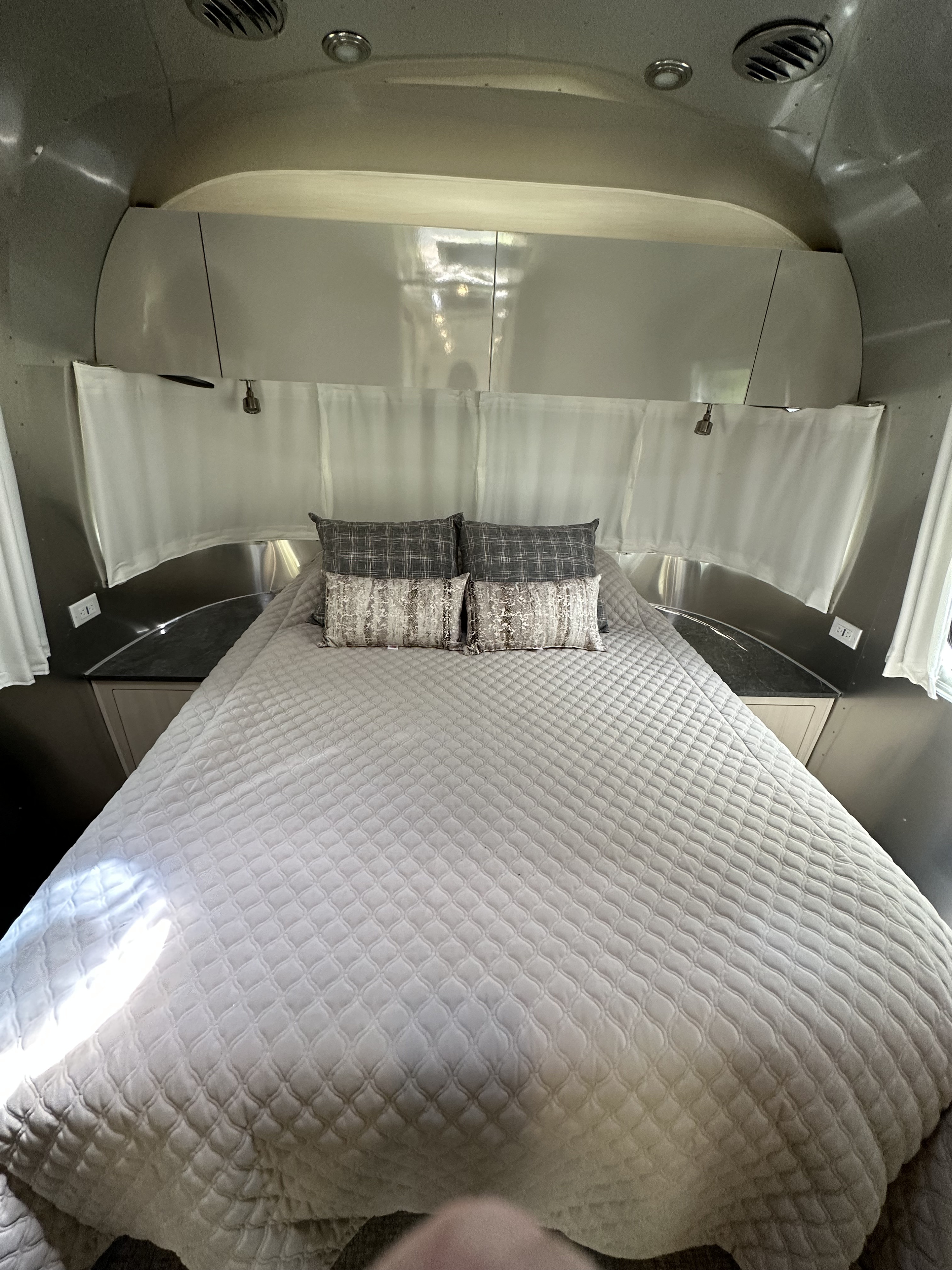 Inside an RV rental: a cozy Airstream bedroom with a large bed, quilted spread, and sleek silver walls. Ready for your trip!. Airstream Flying Cloud 2022