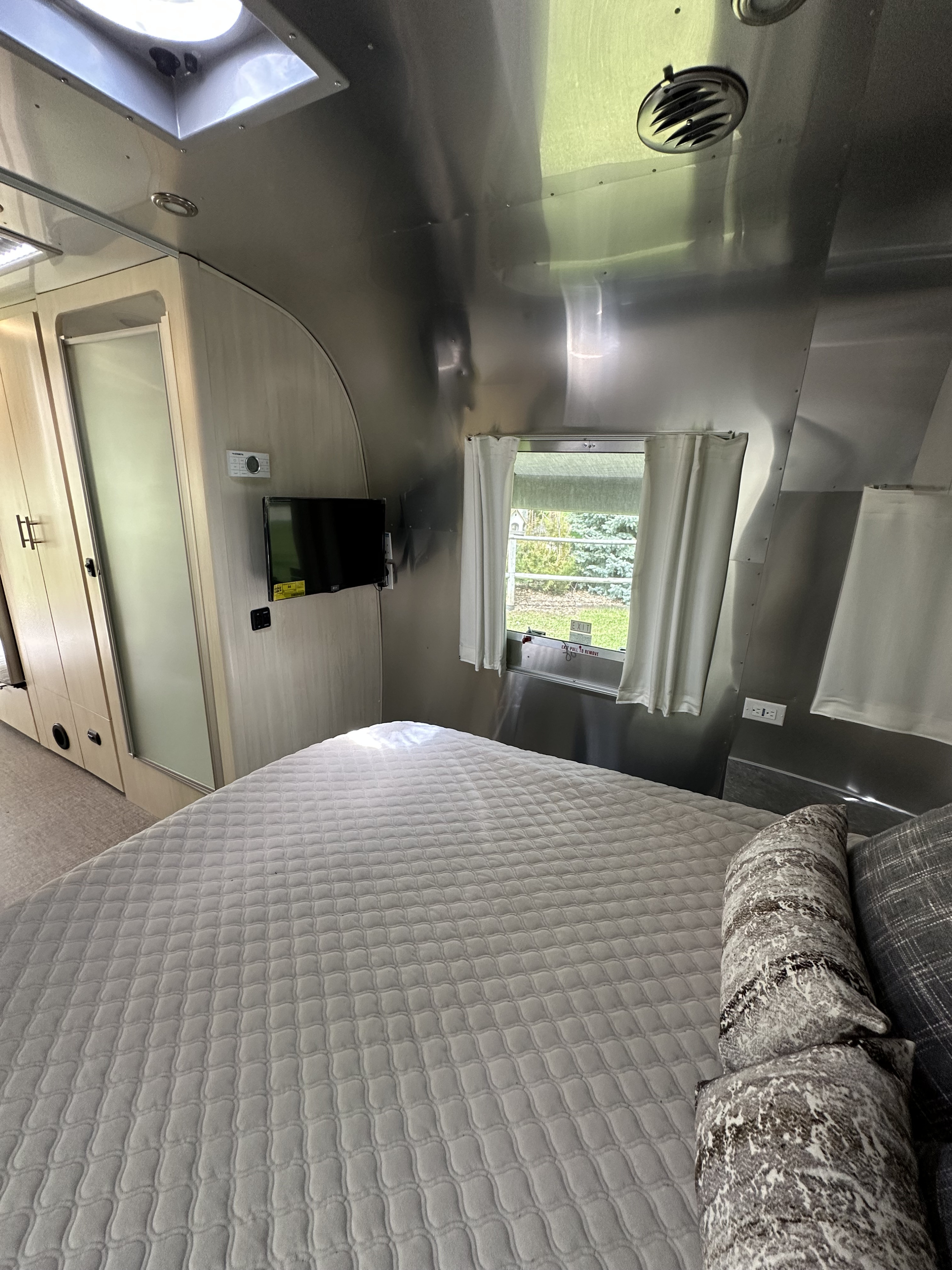 Comfortable RV rental bedroom with a sleek Airstream interior, showing a bed, TV, and a window with greenery outside.. Airstream Flying Cloud 2022