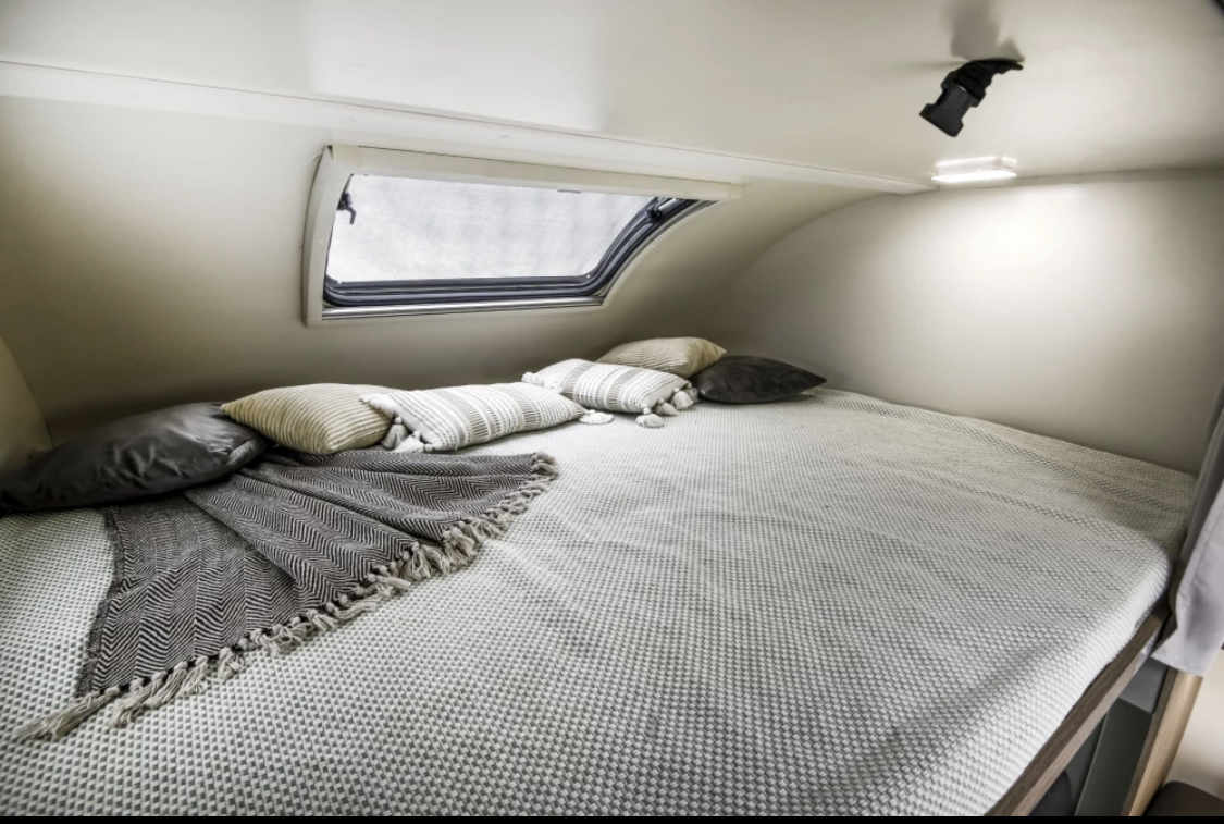 Cozy RV rental bed with textured blanket, soft pillows, and a window for comfortable sleeping.. Roller Team 746 2023
