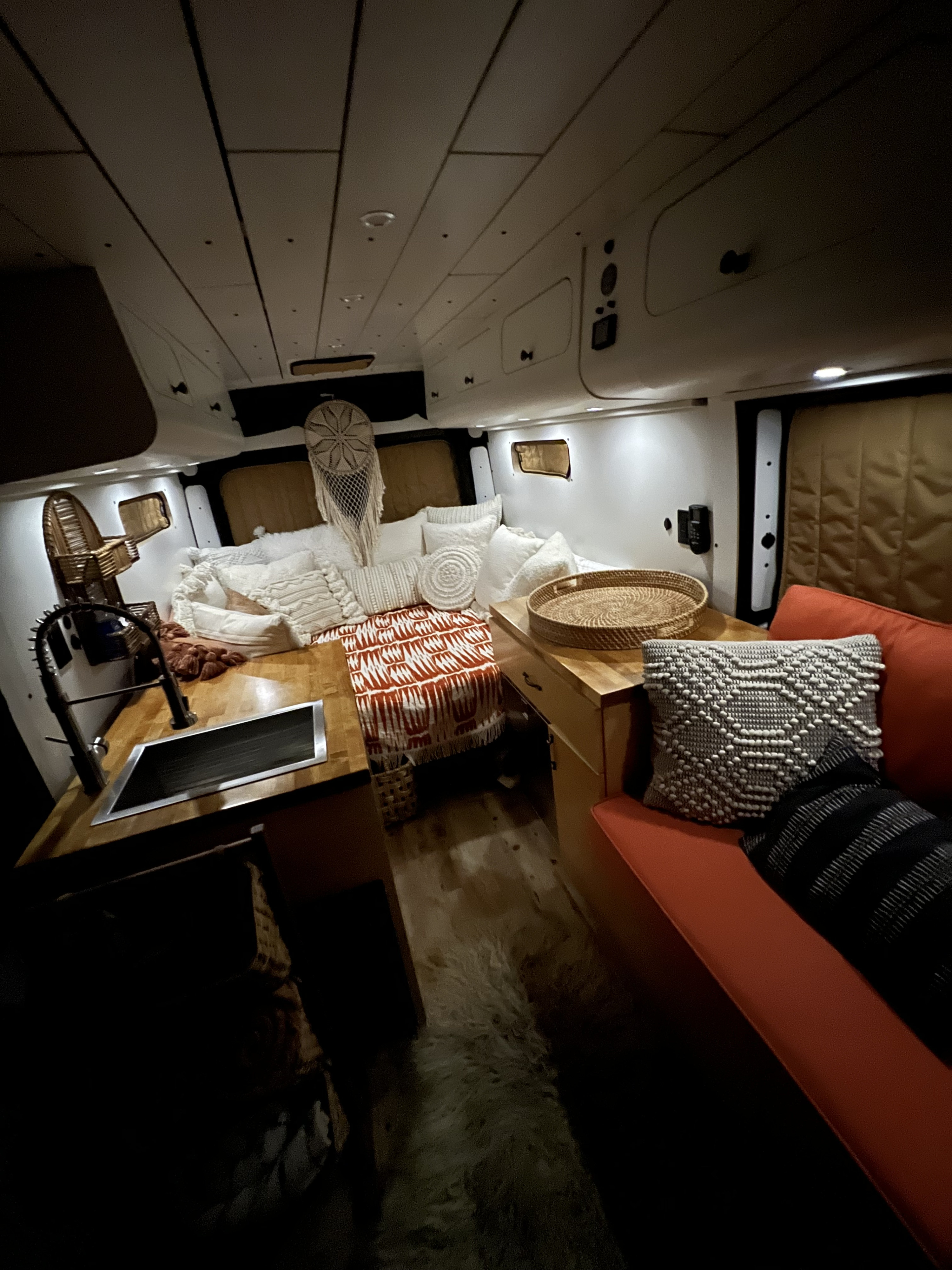 Cozy RV rental interior shows a bed with pillows, kitchen sink, and orange sofa with decorative cushions. Perfect van life setup.. Dodge Ram 1500 2019