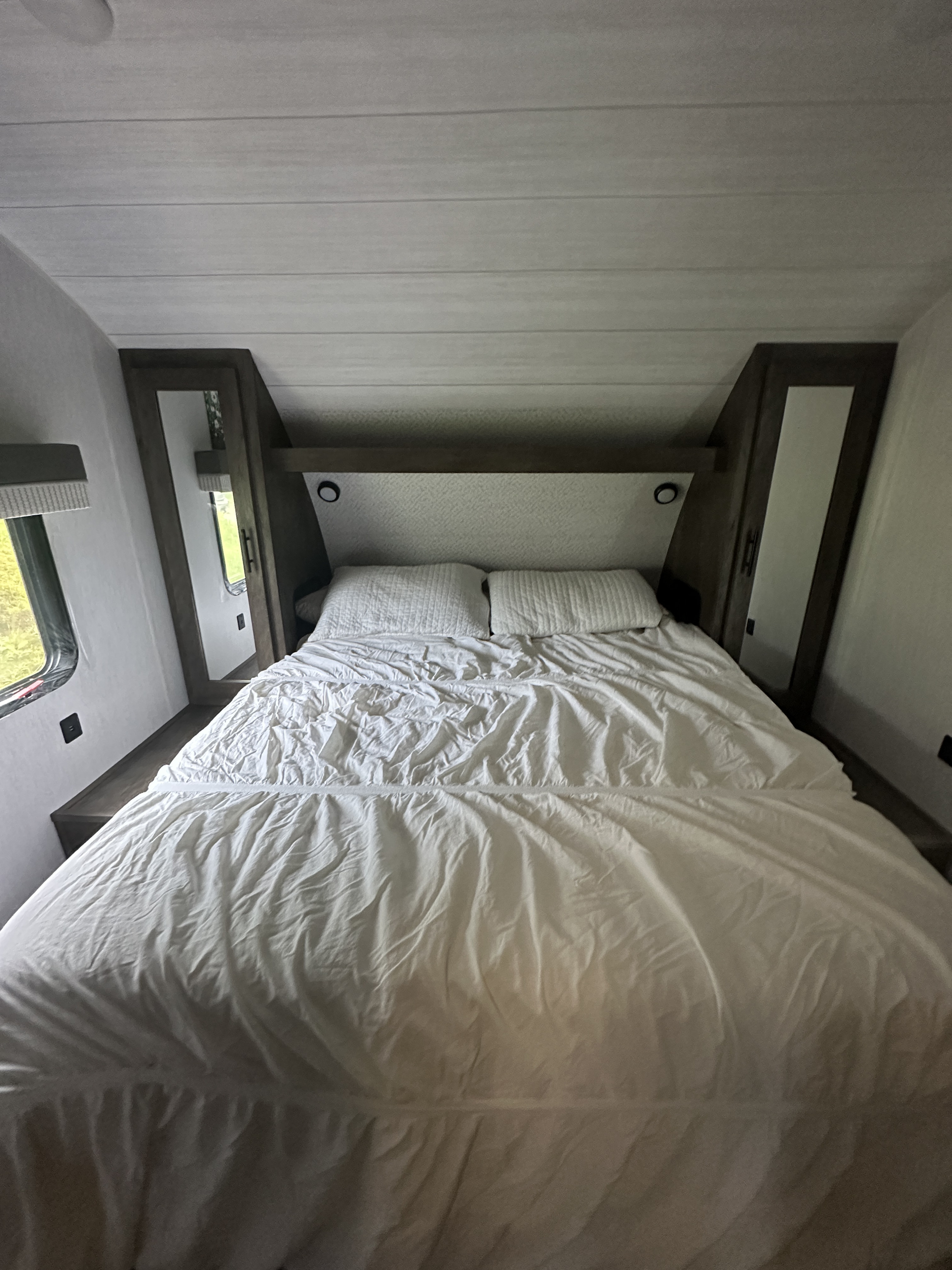 Inside an RV rental, a compact bedroom with a queen bed, white bedding, and built-in storage offers cozy accommodation.. Forest River Salem Cruise Lite 2022