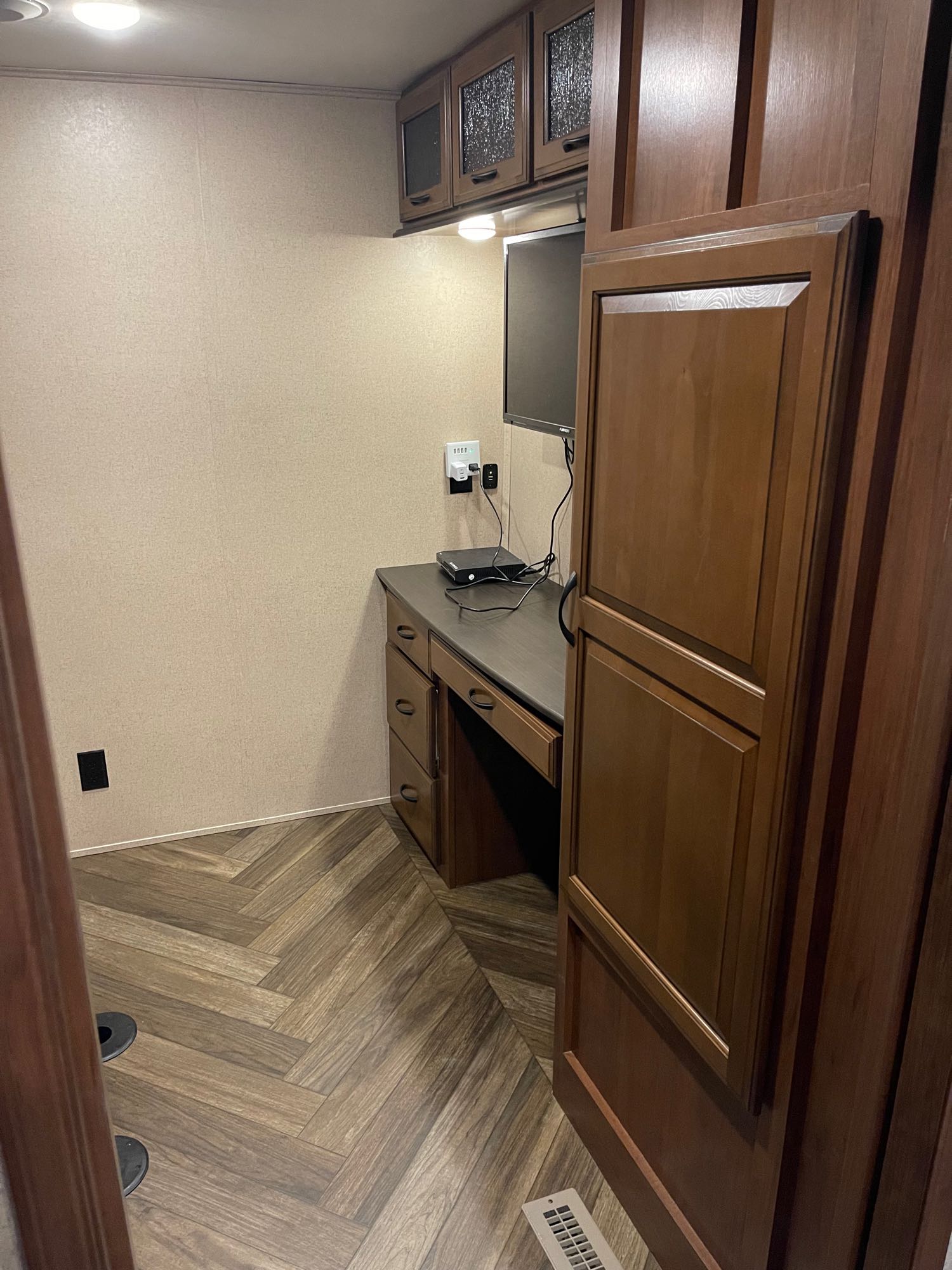 Inside this RV rental, find a functional workspace: a wood desk with drawers, mounted monitor, and cabinets, on herringbone flooring.. Jayco North Point 2017