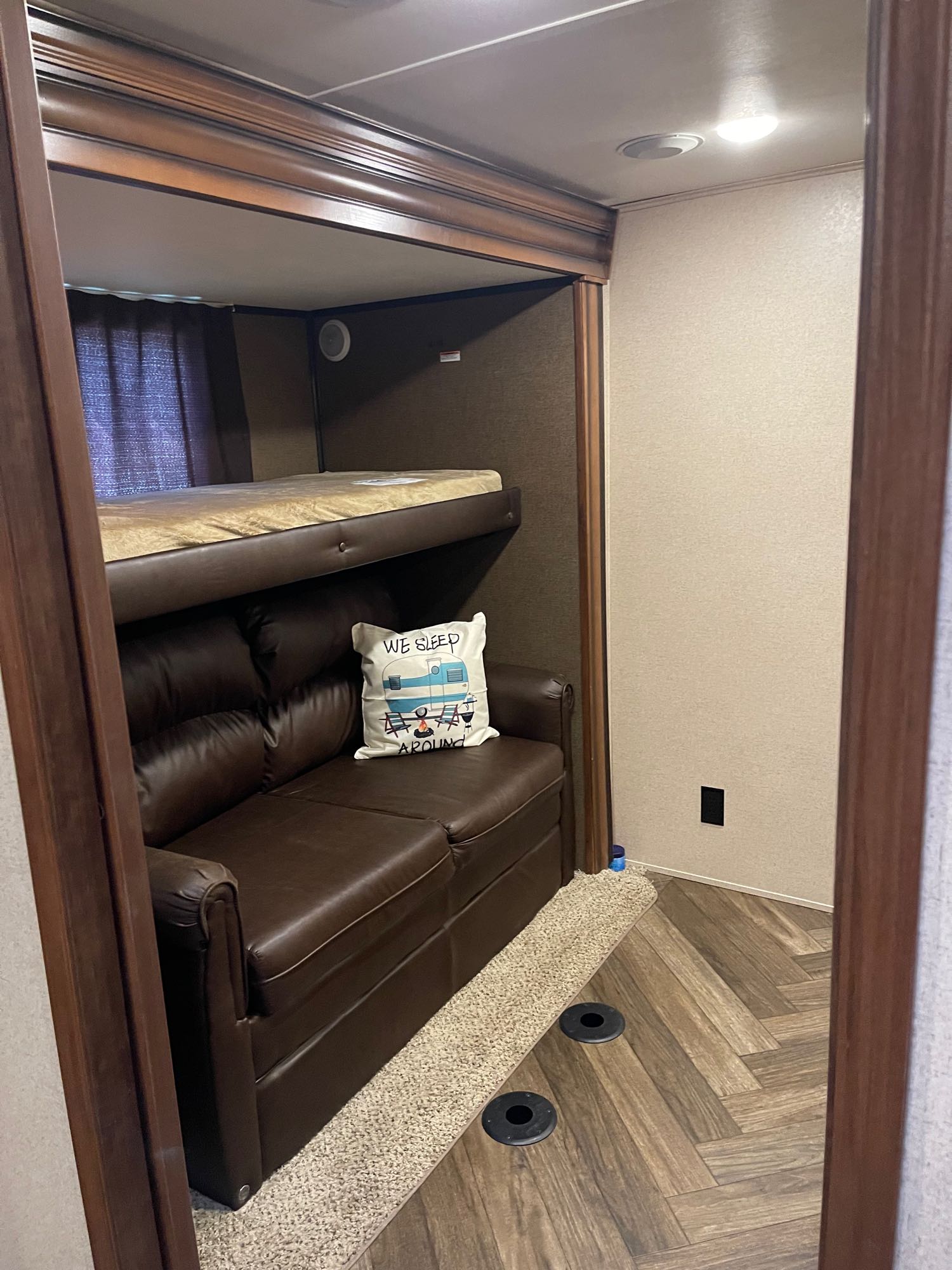 Cozy RV rental interior featuring a brown leather sofa, an upper bunk bed, and wood-look flooring. Perfect compact living.. Jayco North Point 2017
