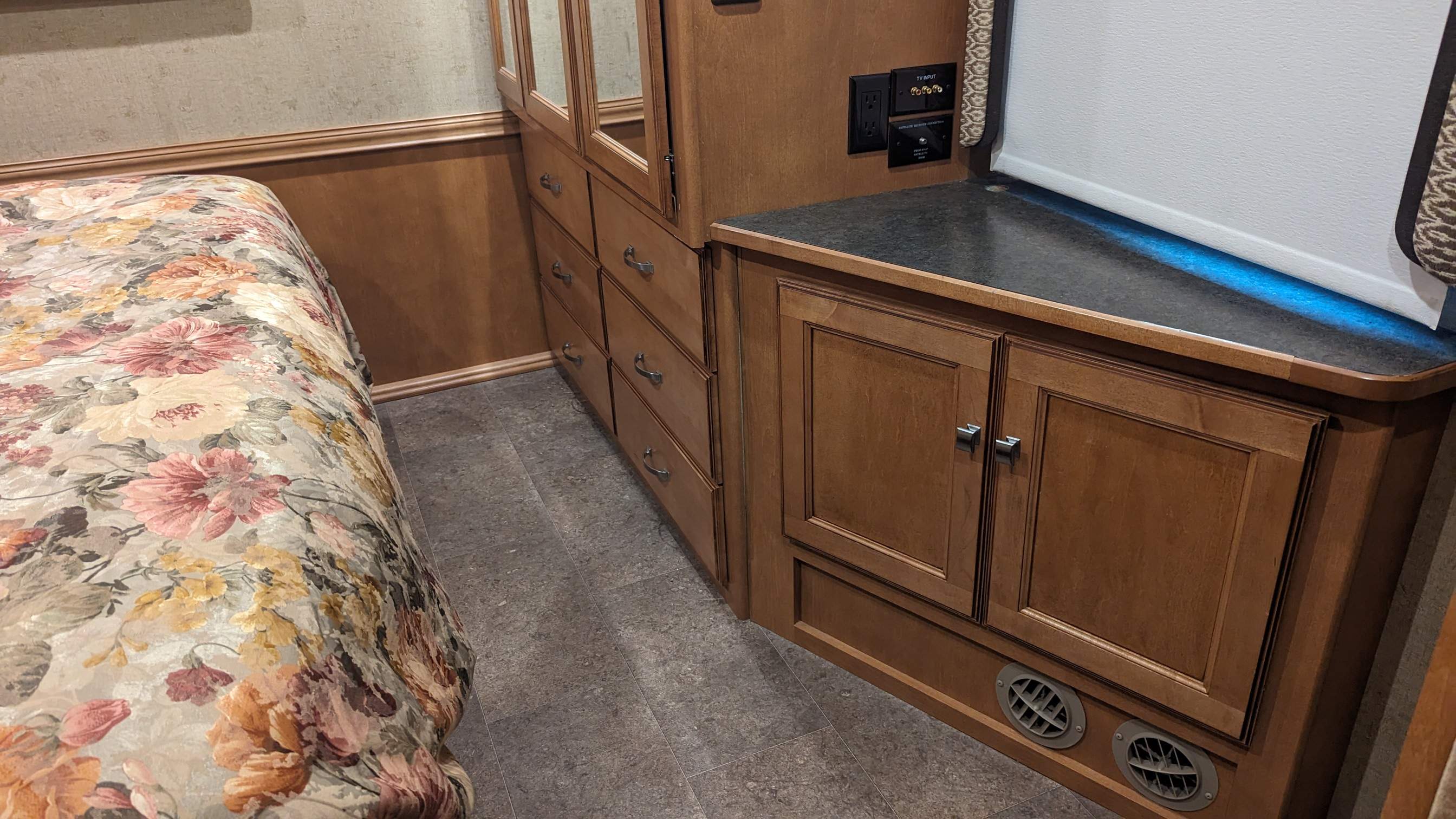 RV rental interior: bedroom with floral bed, wood storage cabinets, power outlets, TV input, and floor vents.. Itasca Sunova 2014