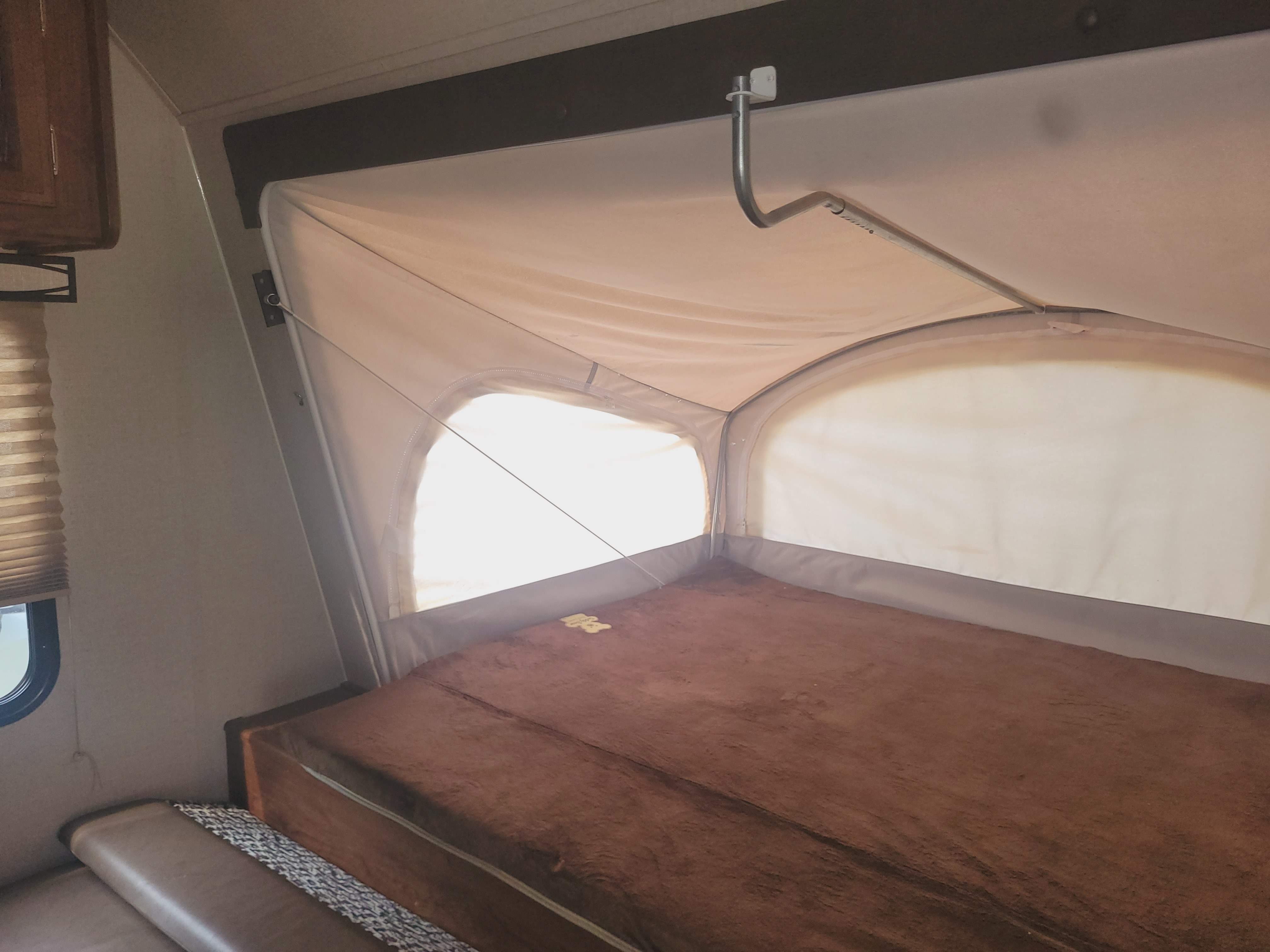 Spacious pop-out bed in an RV rental, featuring soft fabric walls and bright windows. A cozy sleeping area for your camper adventure.. Coachmen Freedom Express Hybrid 2018