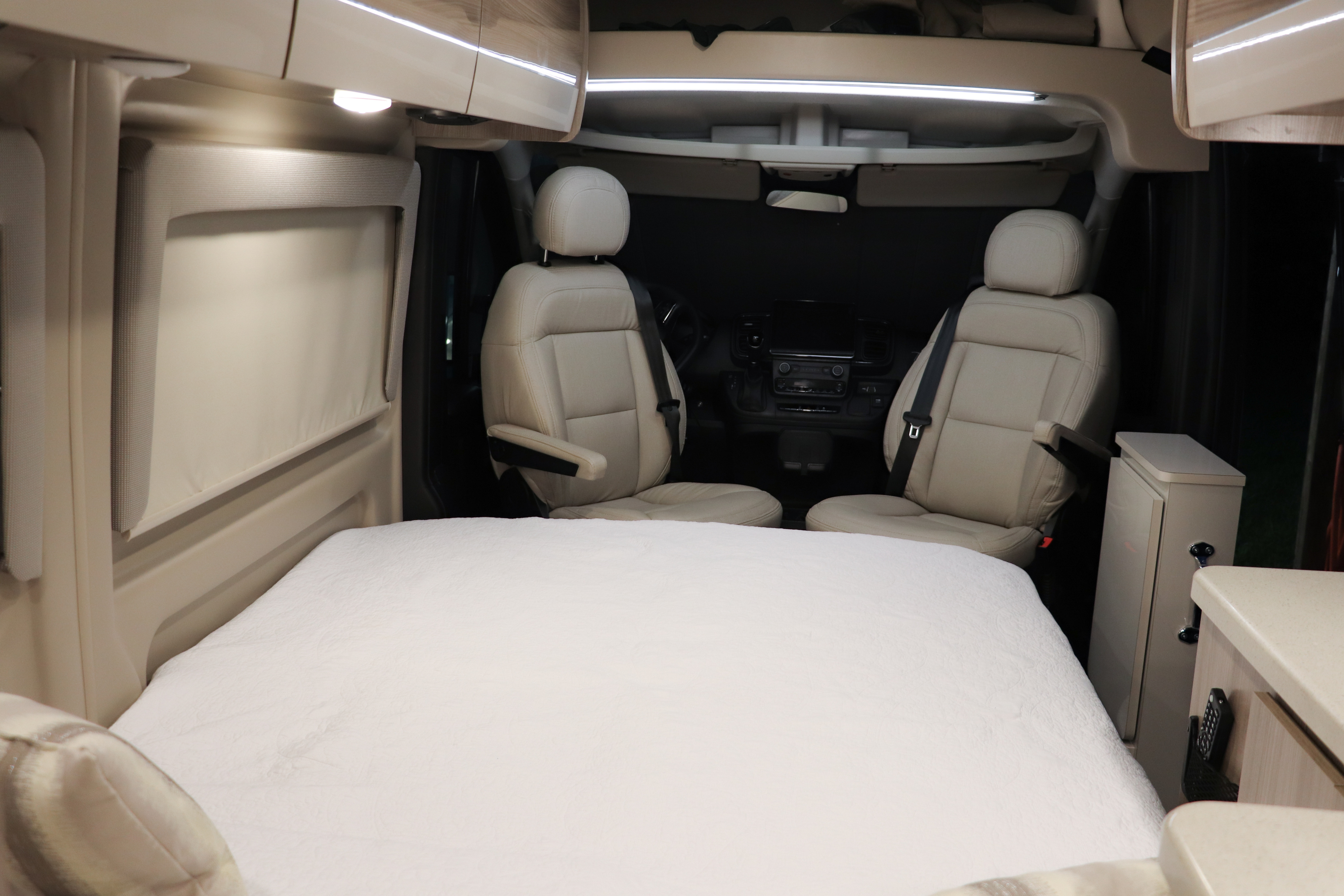 Cozy RV rental interior: a bed in the foreground, leading to the light-colored front seats & dashboard.. Thor Sequence 20K 2024