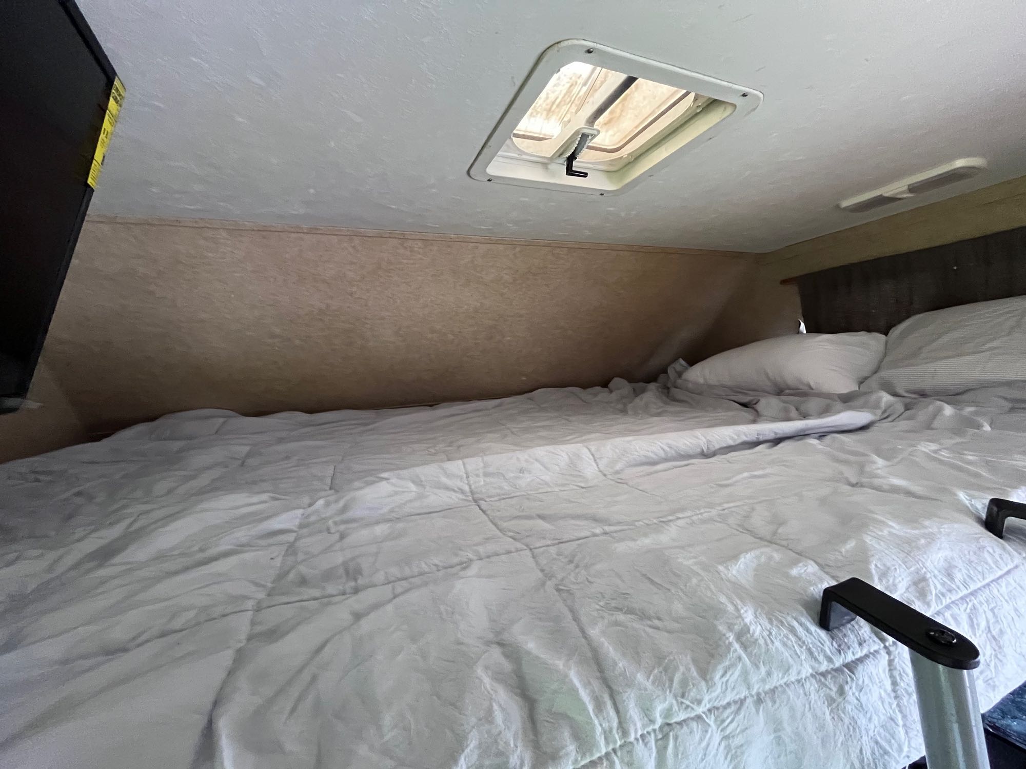 Comfortable RV rental sleeping area, with a large bed, pillows, a ceiling vent, and a mounted TV.. Thor Majestic 2017