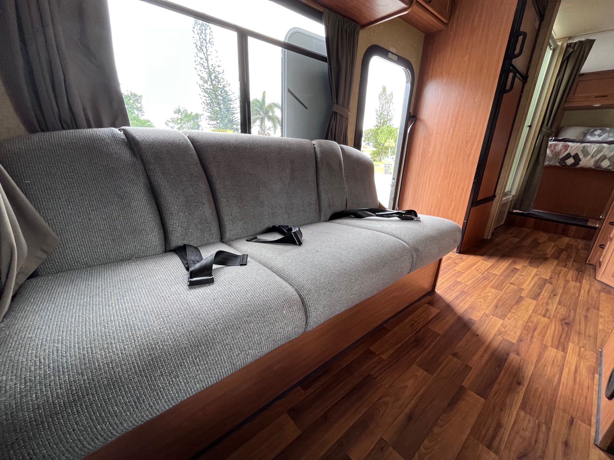 Inside this RV rental: Features include a grey sofa with seatbelts, wood floors, large windows, and a bunk.. Thor Majestic 2017