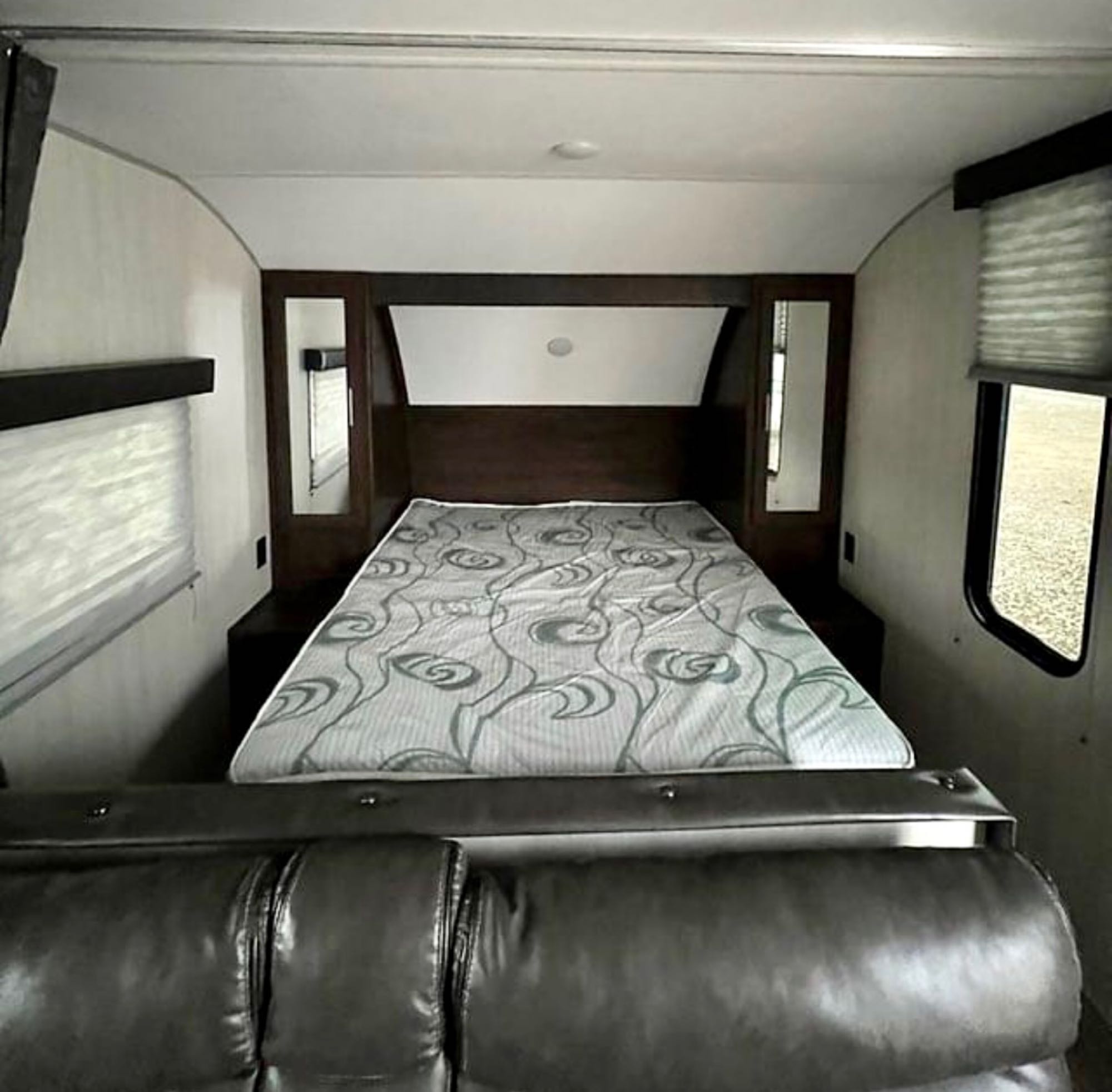 Explore this cozy RV rental's bedroom, featuring a comfortable bed with a patterned cover and a modern leather sofa. Ideal for travel adventures.. Forest River Cherokee Grey Wolf Special Edition 2020