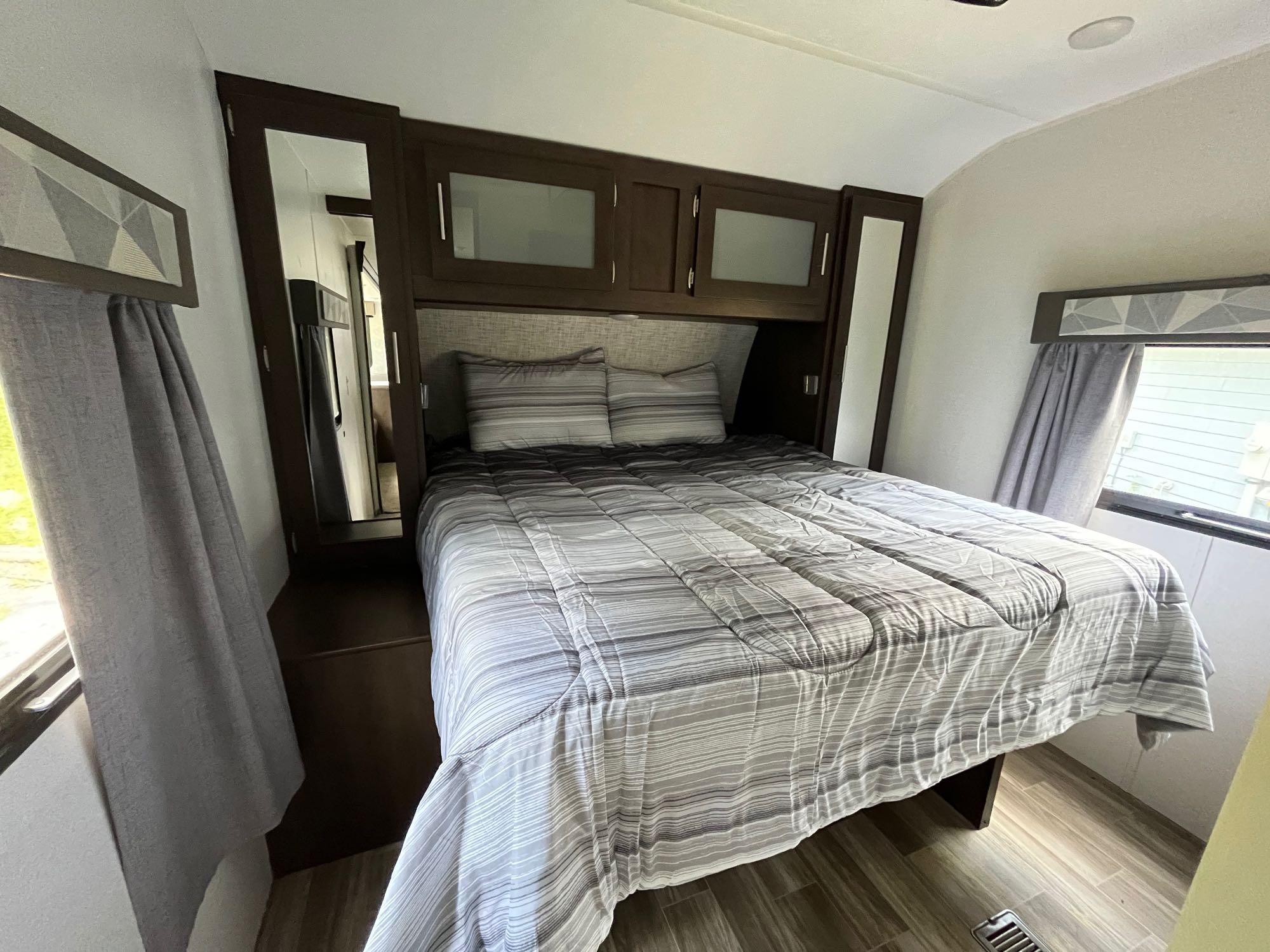 Comfortable RV rental bedroom featuring a striped bed, overhead cabinets, and mirrored wardrobes for your journey.. Forest River Wildwood 2019