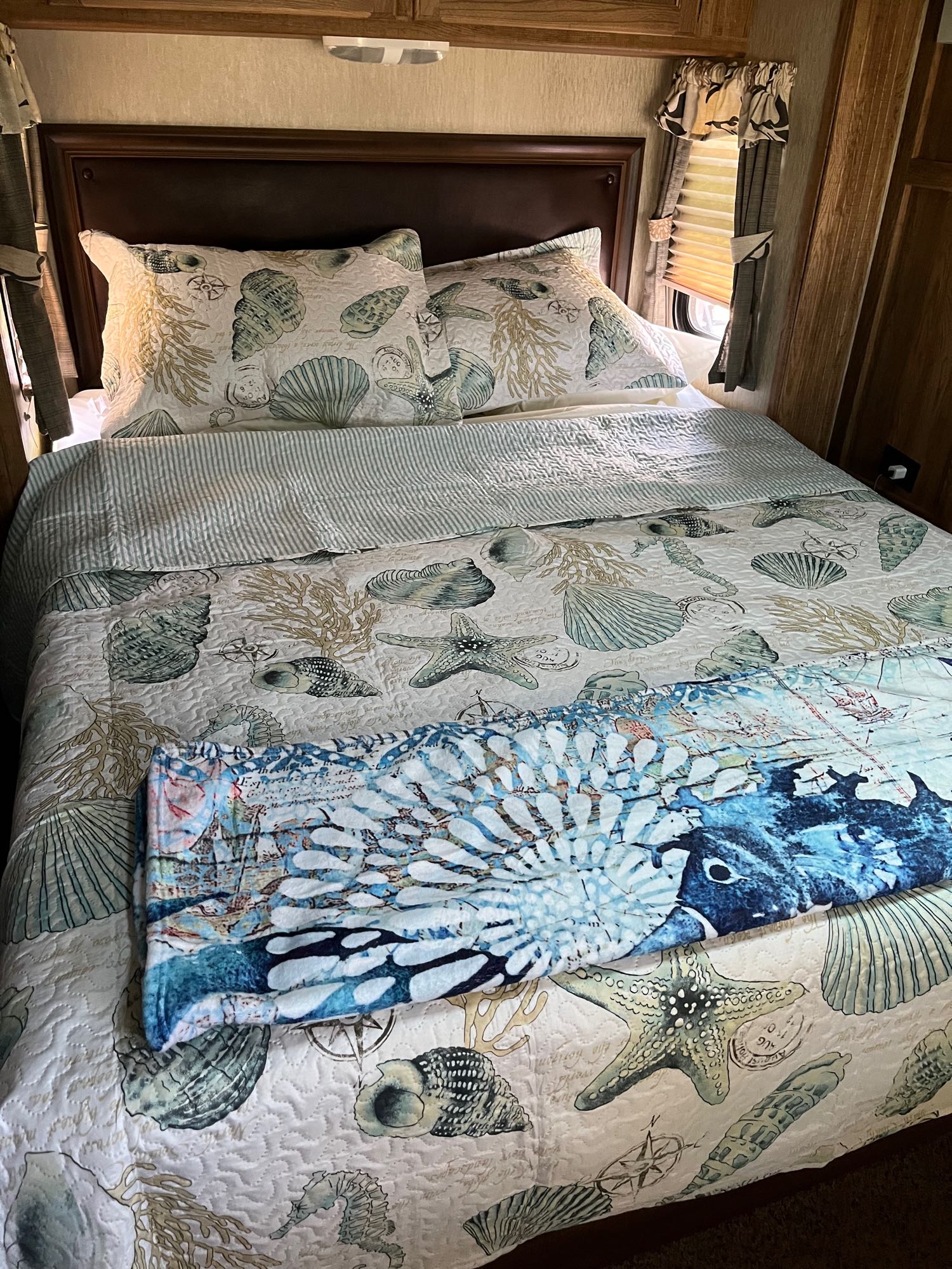 Coastal-themed RV rental bedroom with quilted seashell and starfish bedding, wood headboard, and cabinets.. Keystone Laredo 2015