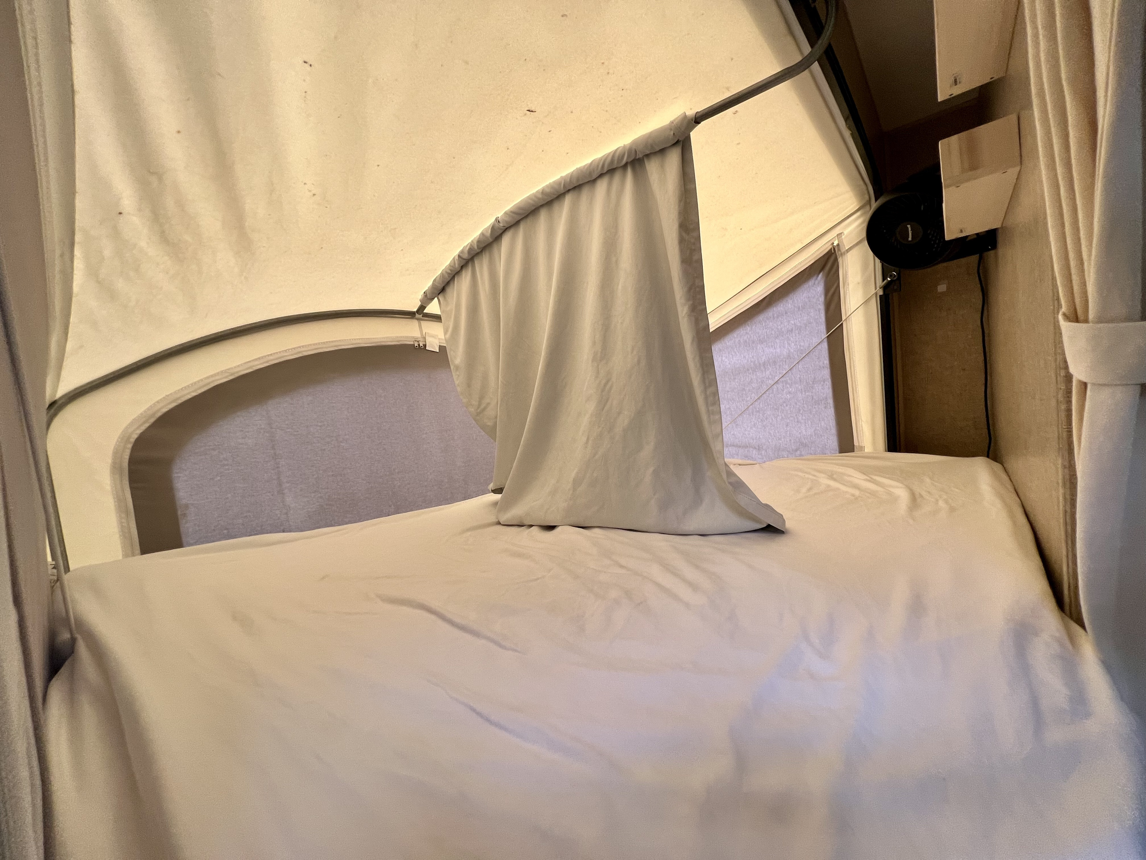 Cozy sleeping area in an RV rental, featuring a neatly made bed with light sheets, a privacy curtain, and fabric walls.. Sportsmen Classic 2015